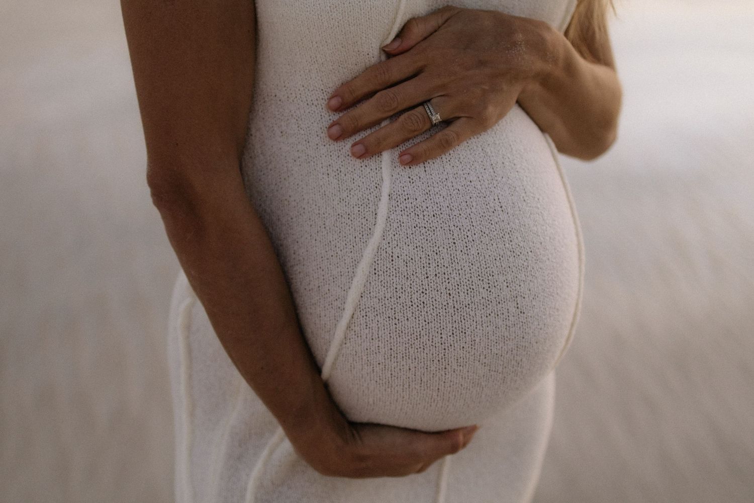 Close-up of pregnant woman in white dress gently holding baby bump.