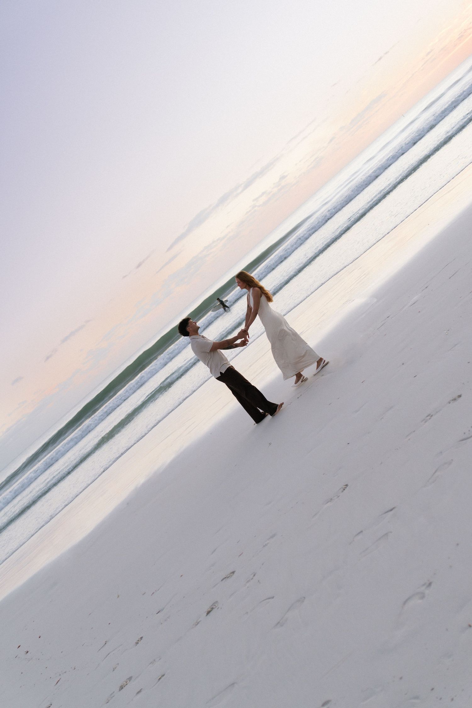 Couple dancing together on white sand beach at sunset near ocean waves.