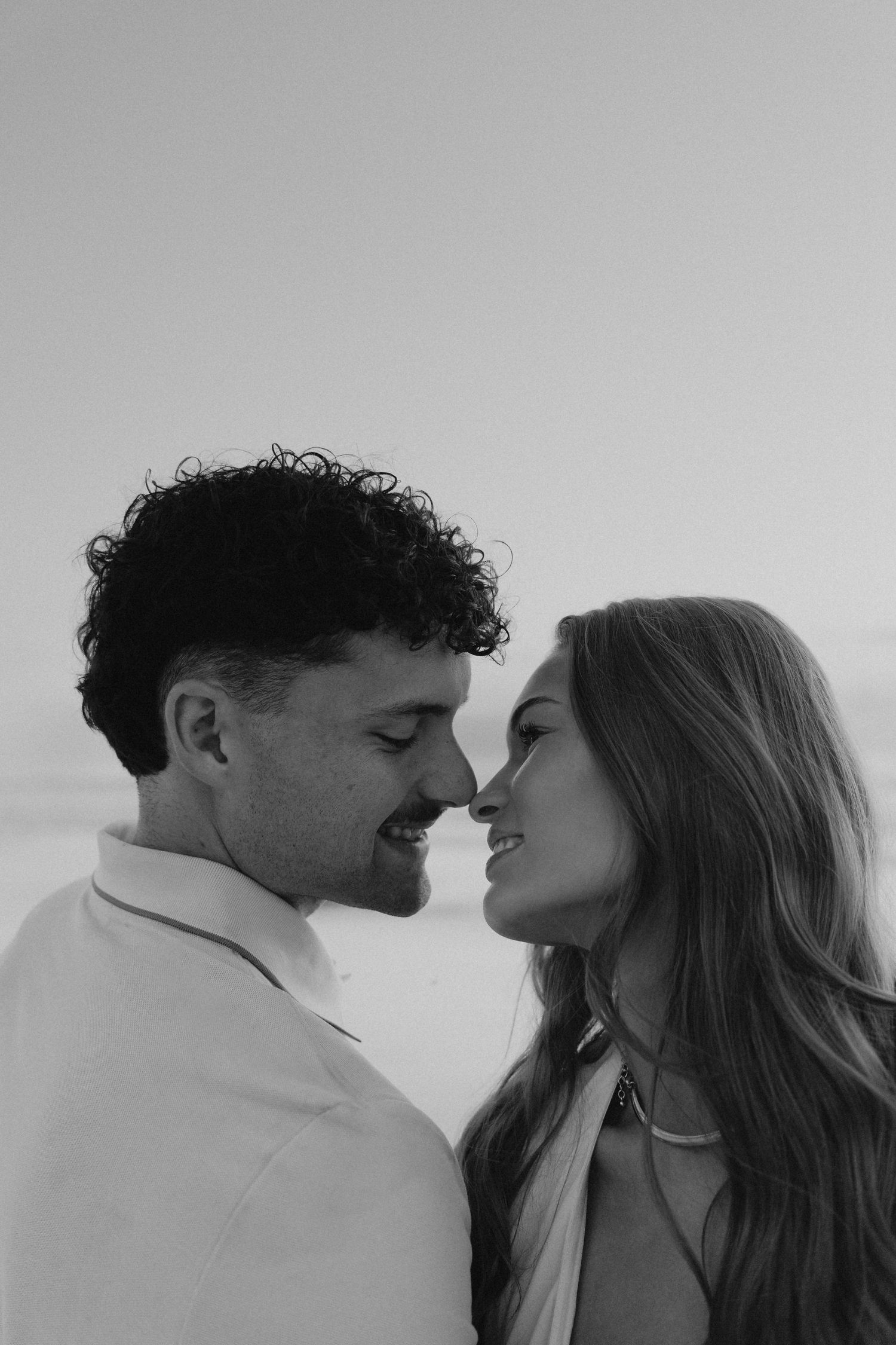Black and white portrait of a happy couple smiling at each other during a beach engagement session.