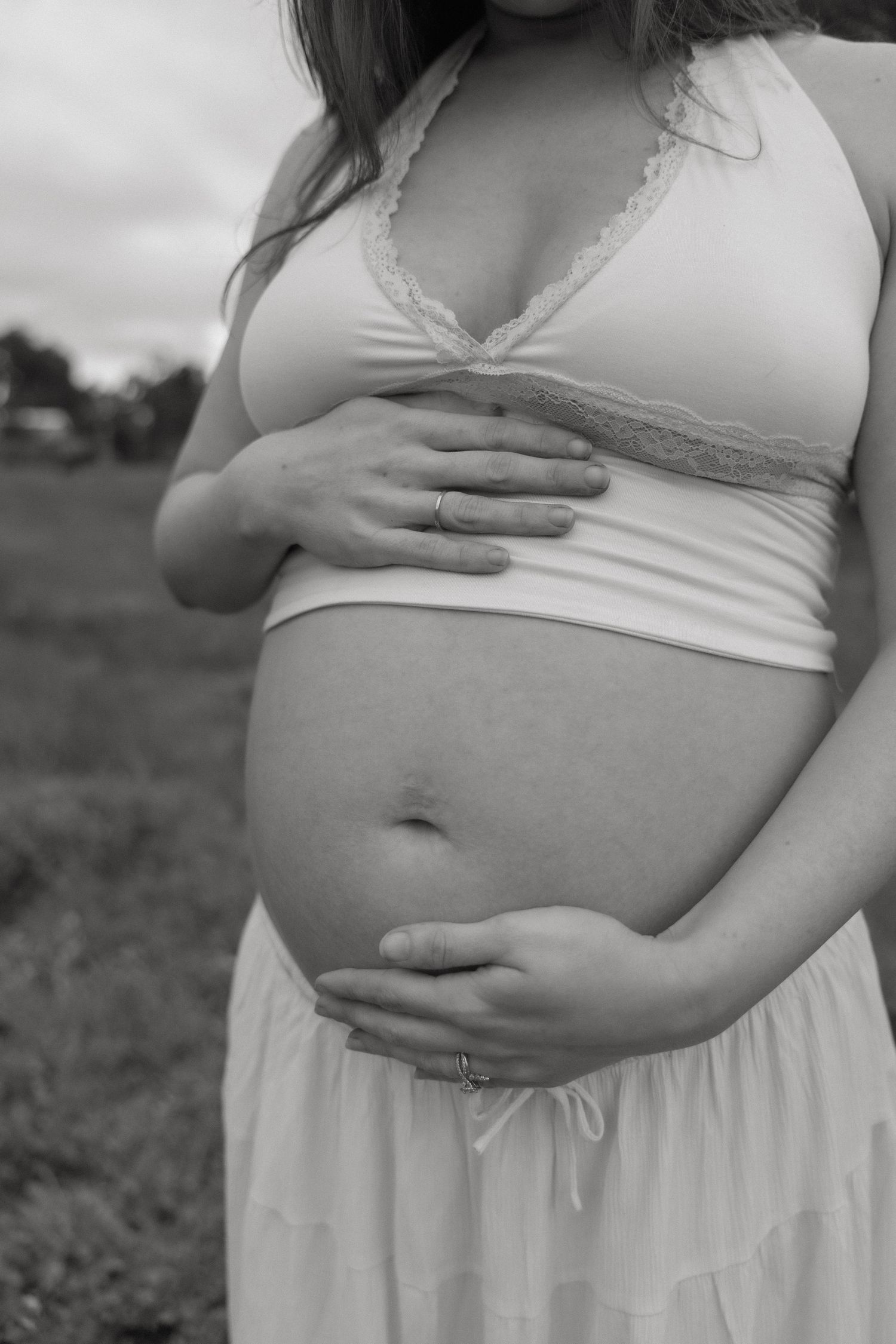 Close-up black and white maternity photo of a pregnant woman cradling her bare baby bump outdoors.