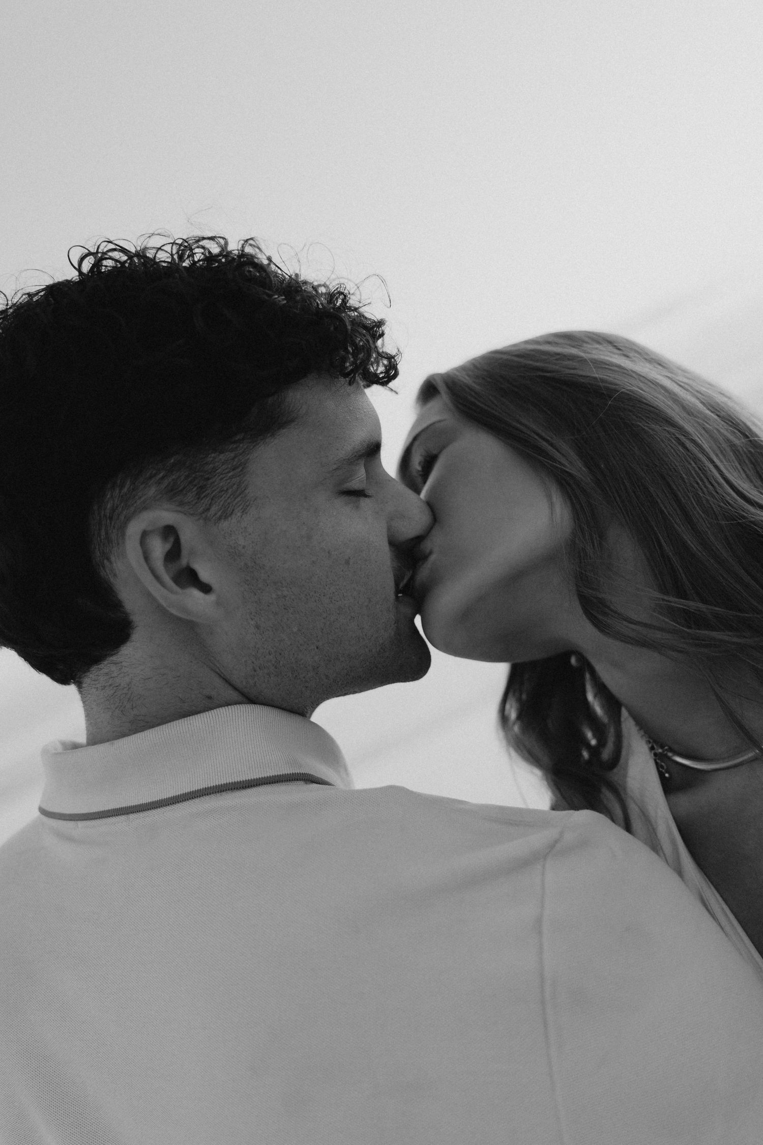 Couple sharing a tender kiss in black and white beach engagement photo at dusk.