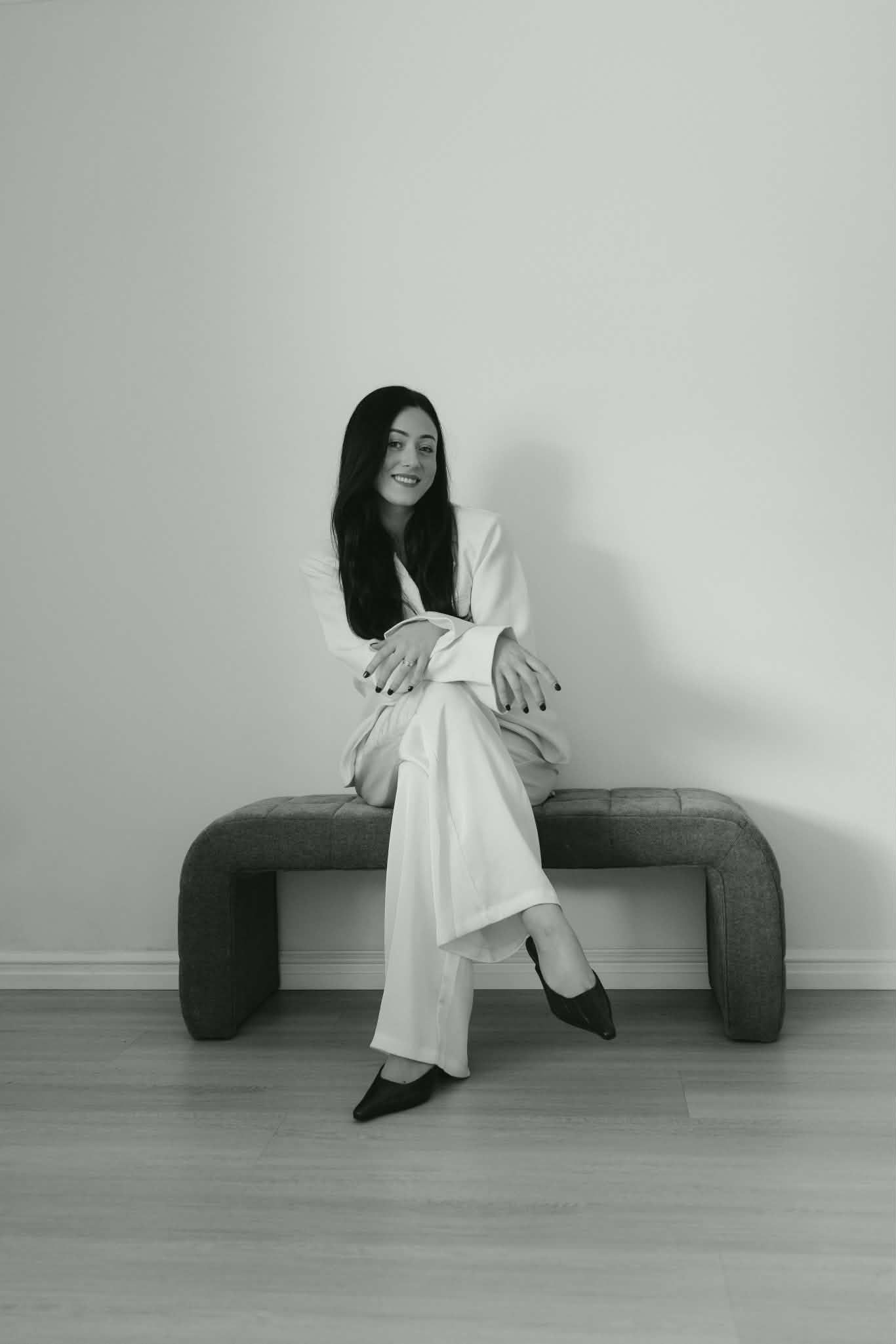 Woman in white suit sitting on bench in black and white portrait.