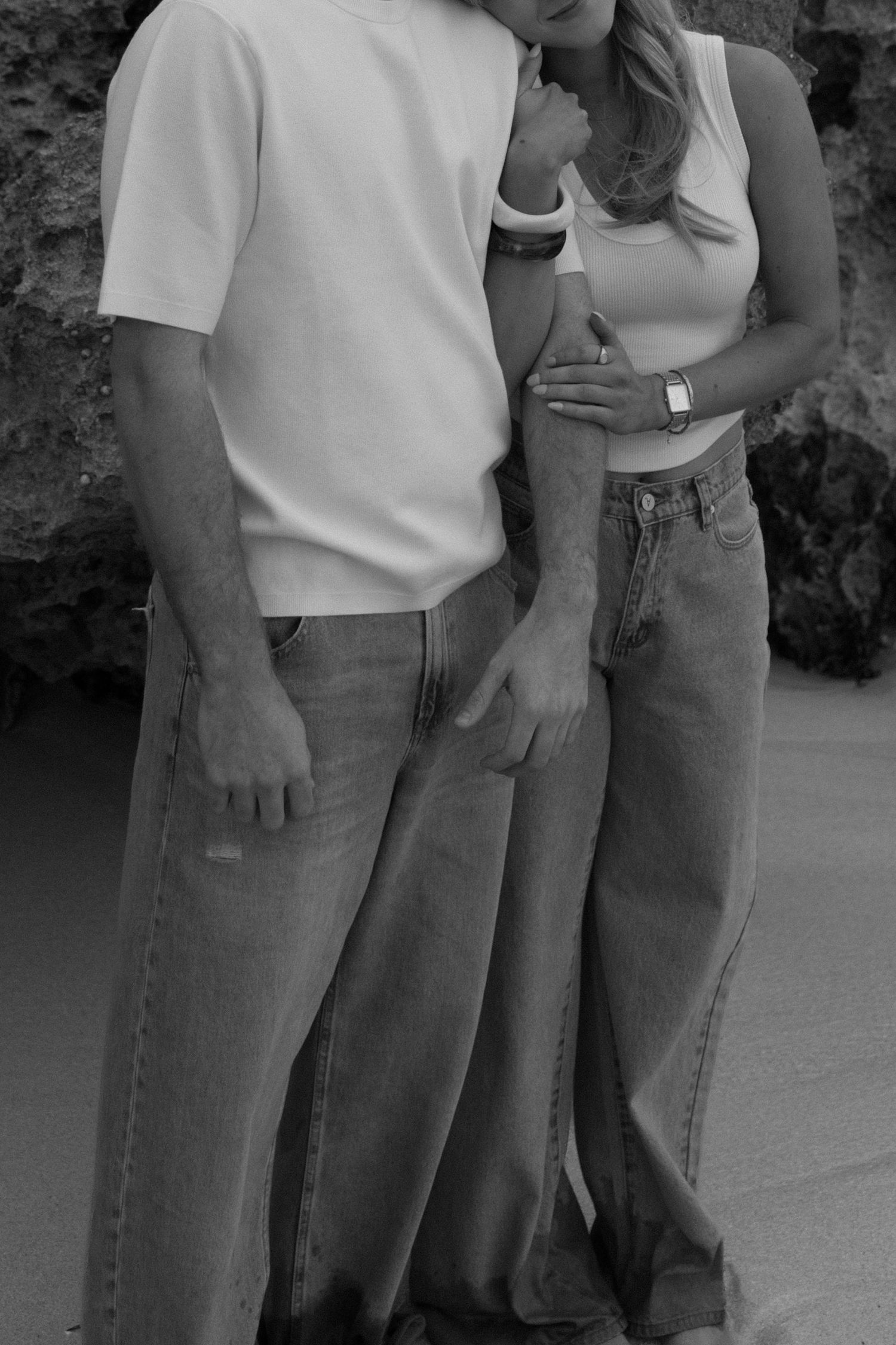 Black and white close-up of couple in jeans and white tops standing together on a beach.