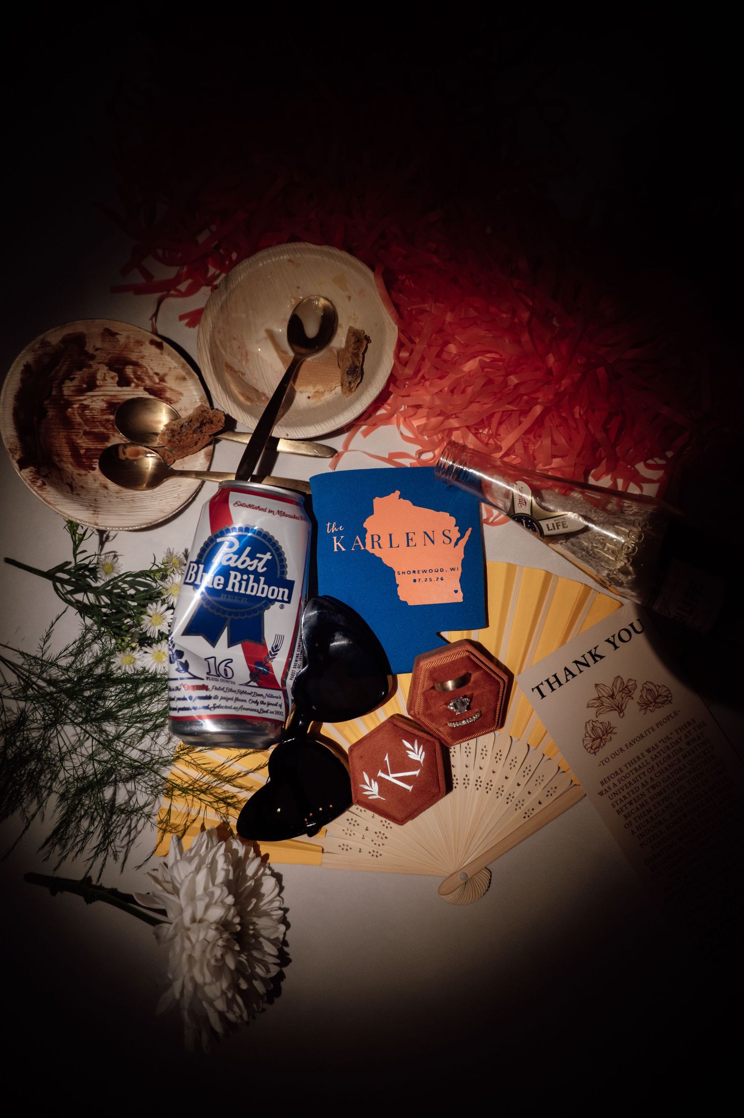 Flatlay of Pabst Blue Ribbon beer, sunglasses, a fan, Karlens Wisconsin booklet, hexagon coasters, and a dessert bowl.