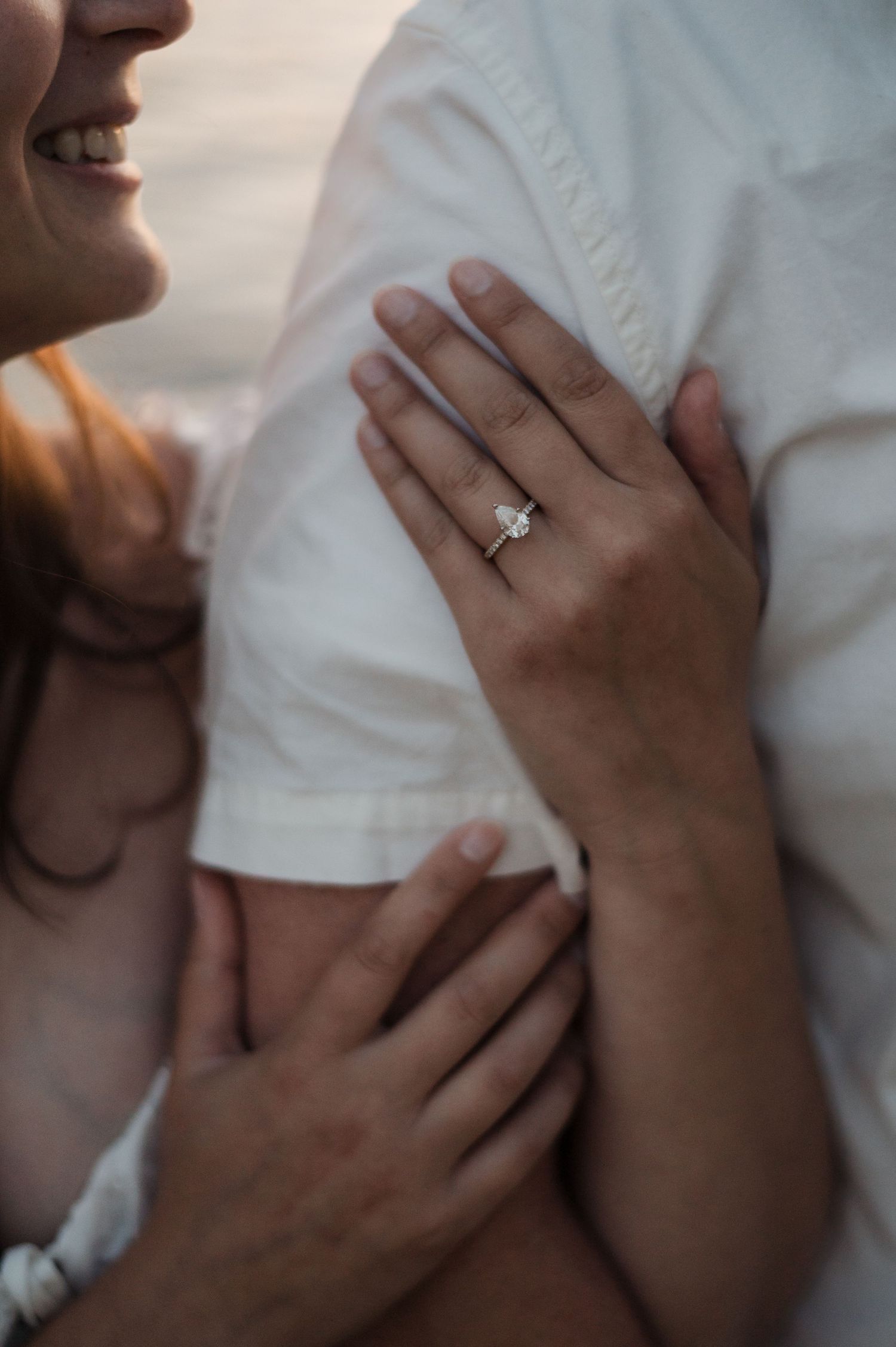 Close-up of womans hand with elegant diamond engagement ring resting on partners white shirt.