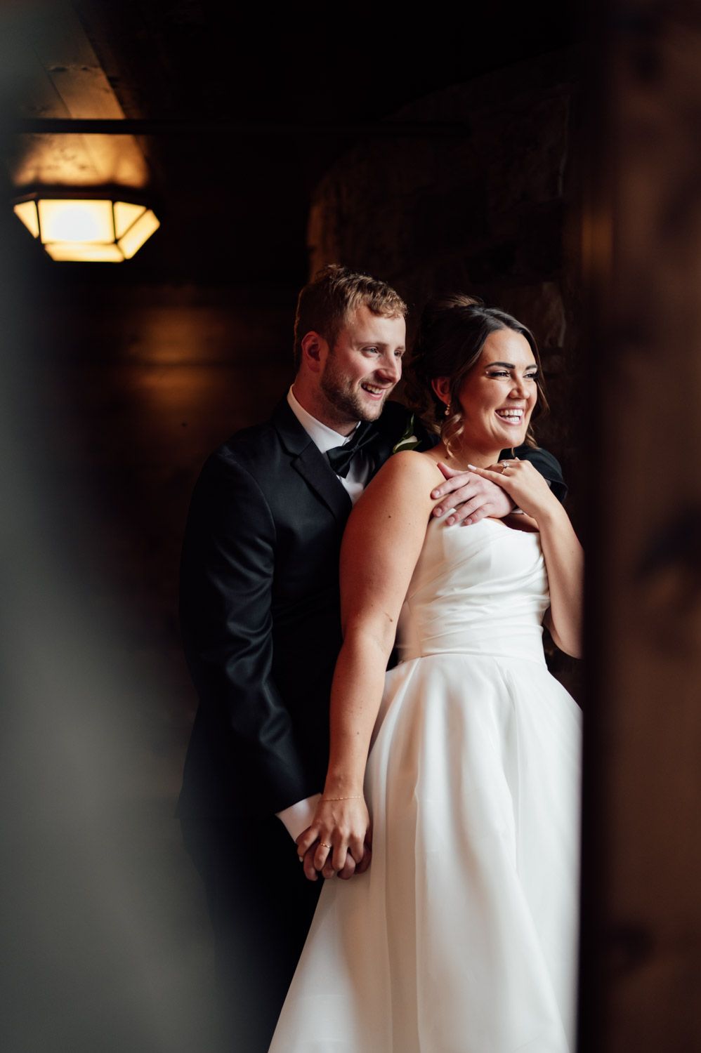 Bride in strapless white gown and groom in black tuxedo posing in romantic candlelit setting.