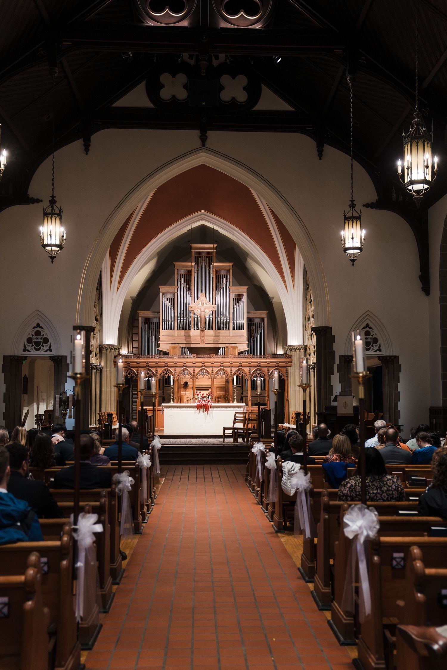 Interior view of a church sanctuary with wooden pews and a pipe organ at the altar under gothic arches.