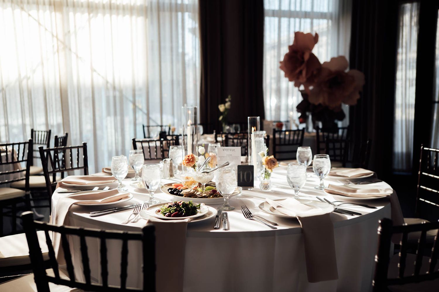 Elegantly set round wedding reception table with white linens, black chairs, and floral centerpieces.