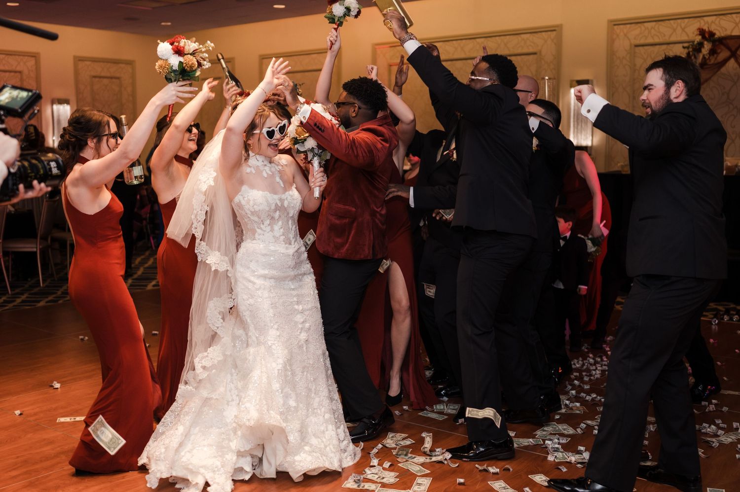 Wedding guests dance and celebrate on a dance floor at a reception while a bride in white dress twirls in the center.
