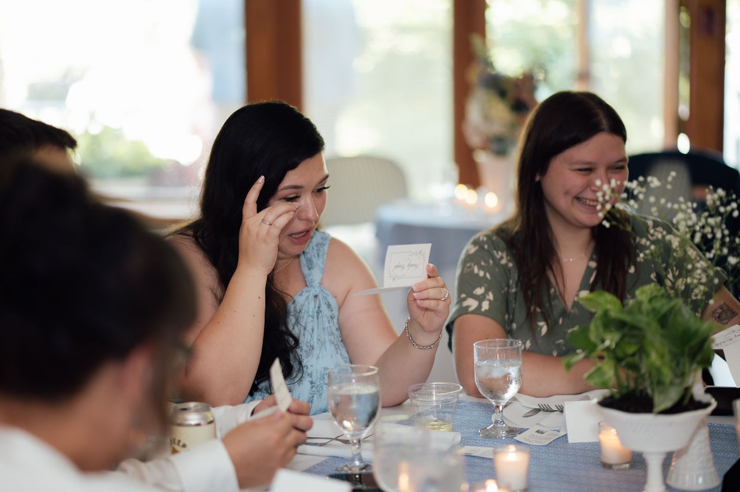 Wedding guests laugh and smile while reading cards at candlelit reception dinner table.