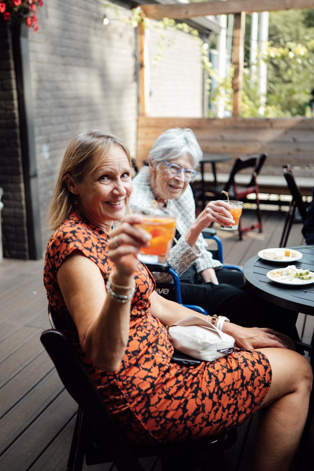 Two women enjoying cocktails on outdoor patio at wedding reception celebration.