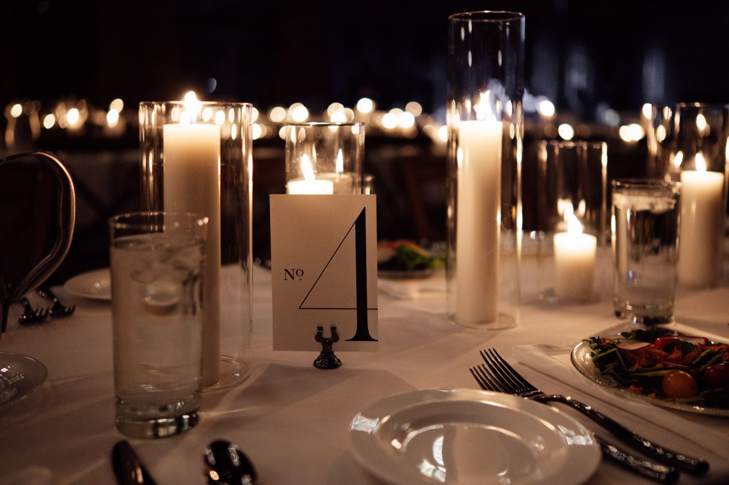 Wedding reception table centerpiece with white pillar candles and elegant table number card.