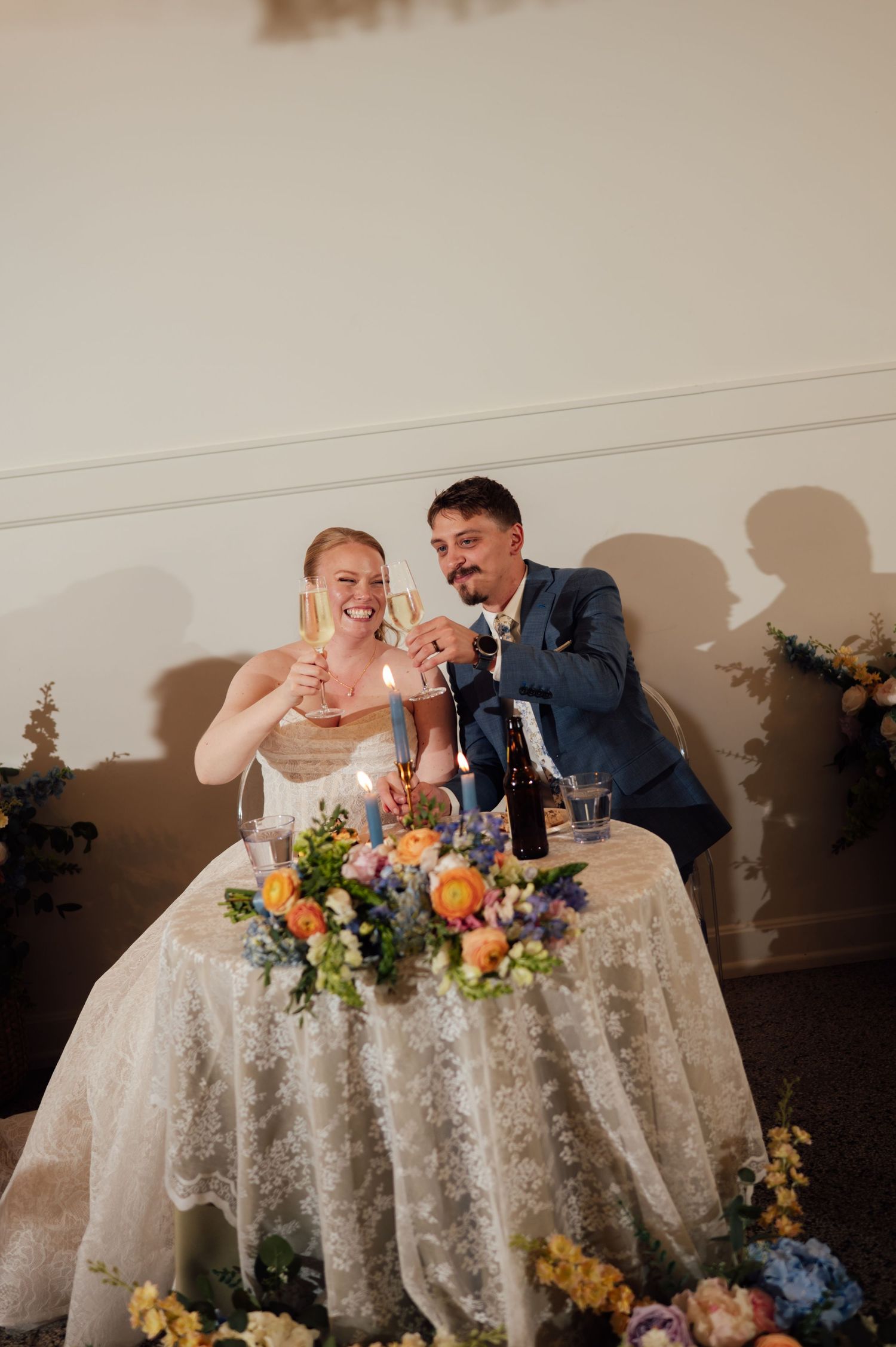 Bride and groom toast champagne at floral sweetheart table during wedding reception.