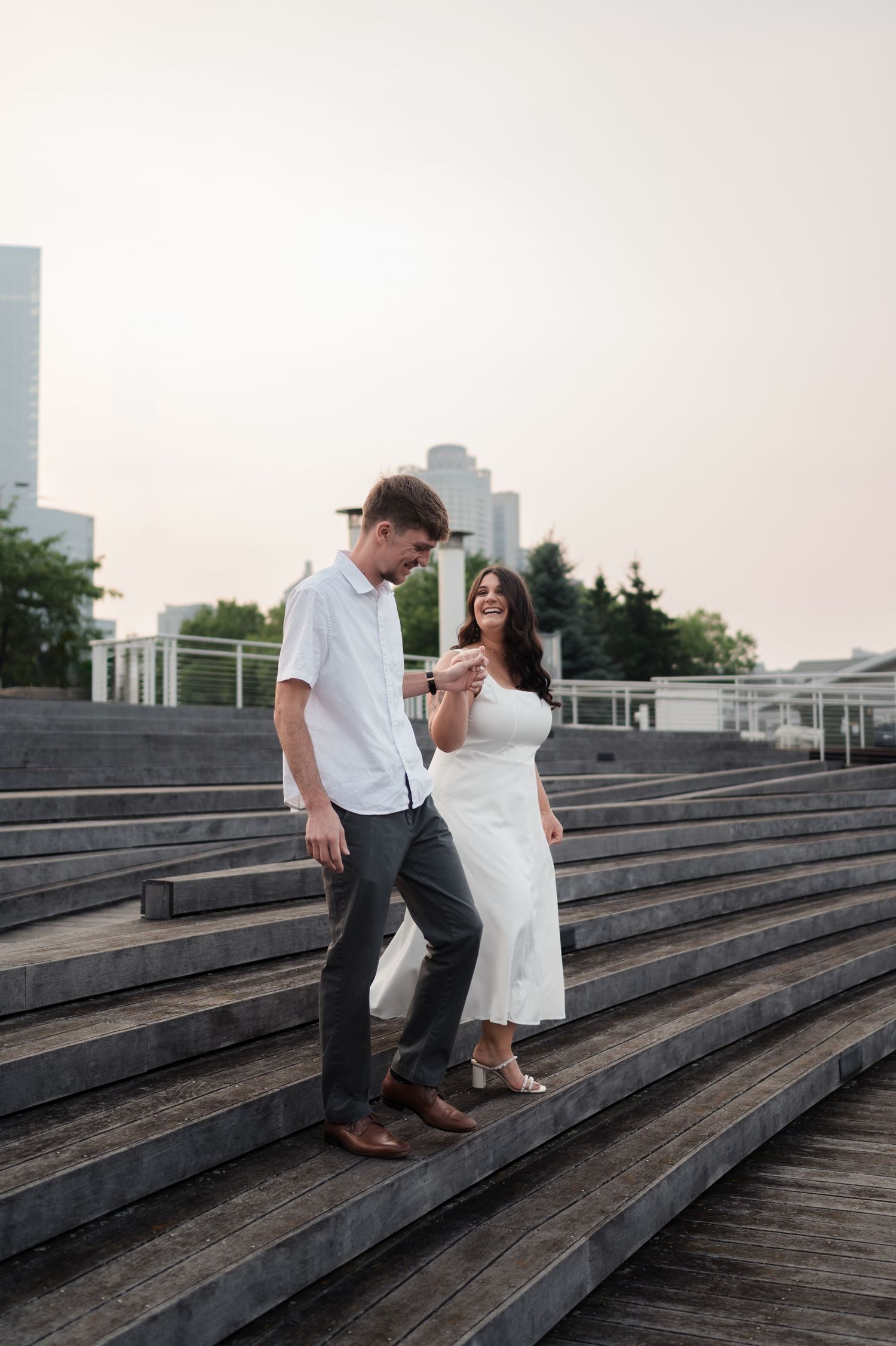 Happy couple walks down wide outdoor steps holding hands, laughing together at golden hour.
