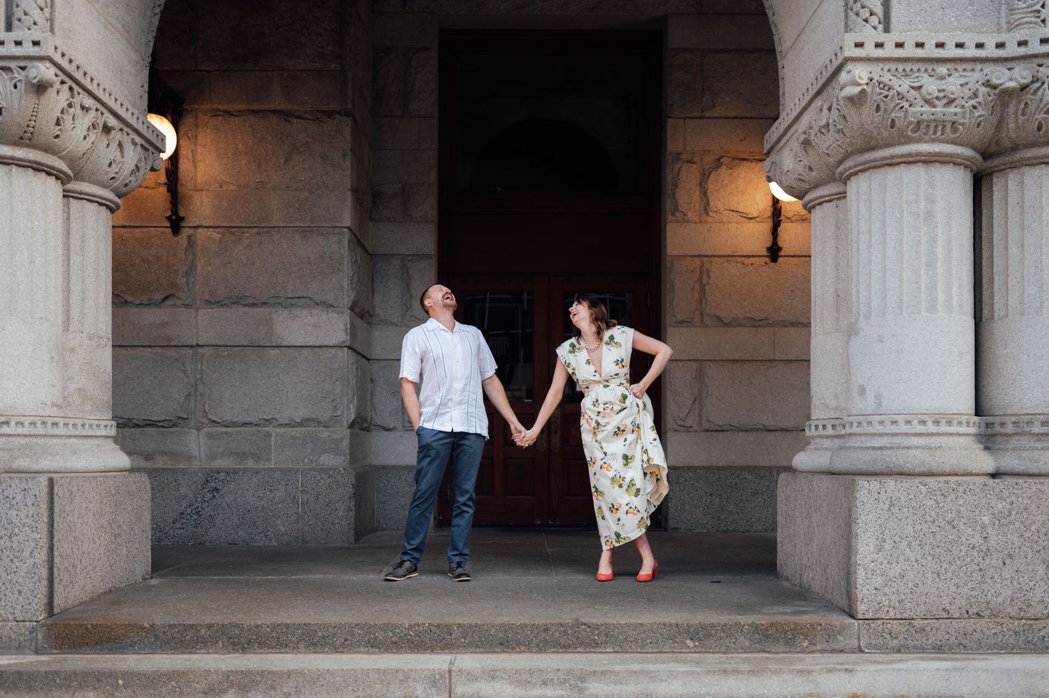 Couple holding hands on stone steps of elegant classical building with tall columns.