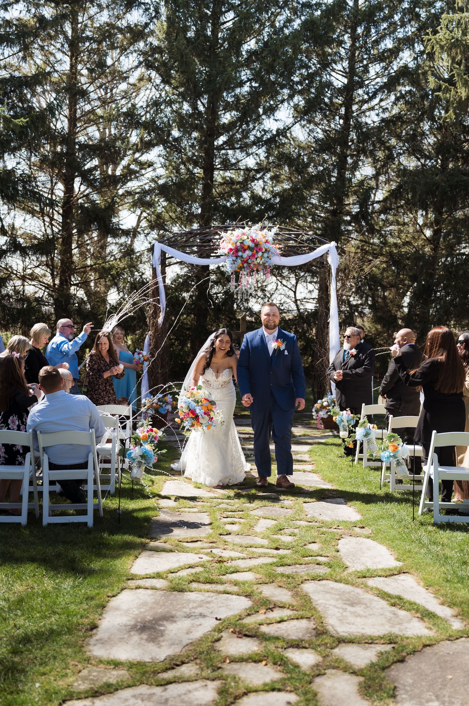 A outdoor wedding ceremony at a forest venue with a decorated arch and stone pathway leading down the aisle.