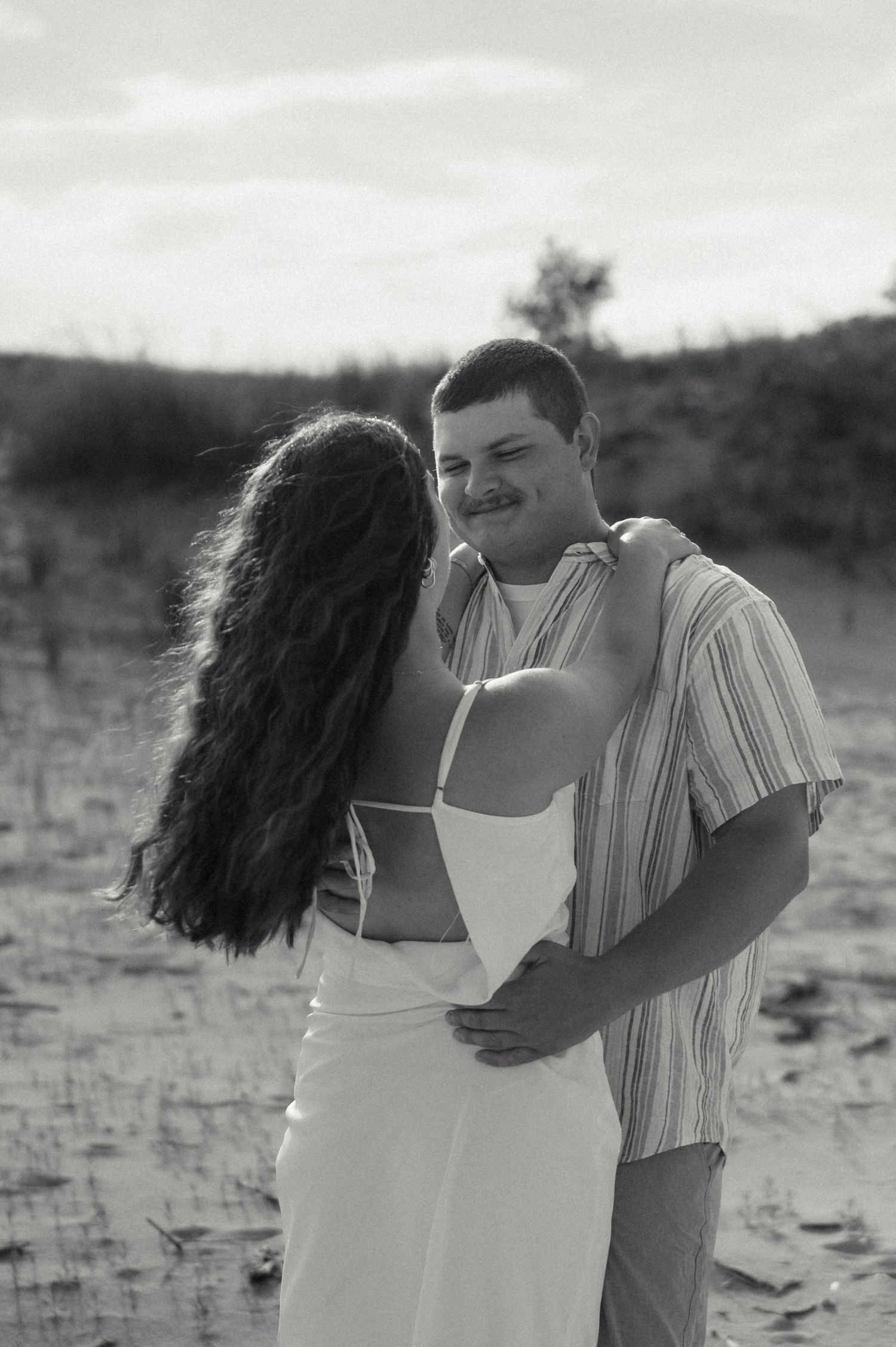 A loving couple embraces on a beach in black and white as they share an intimate moment together.
