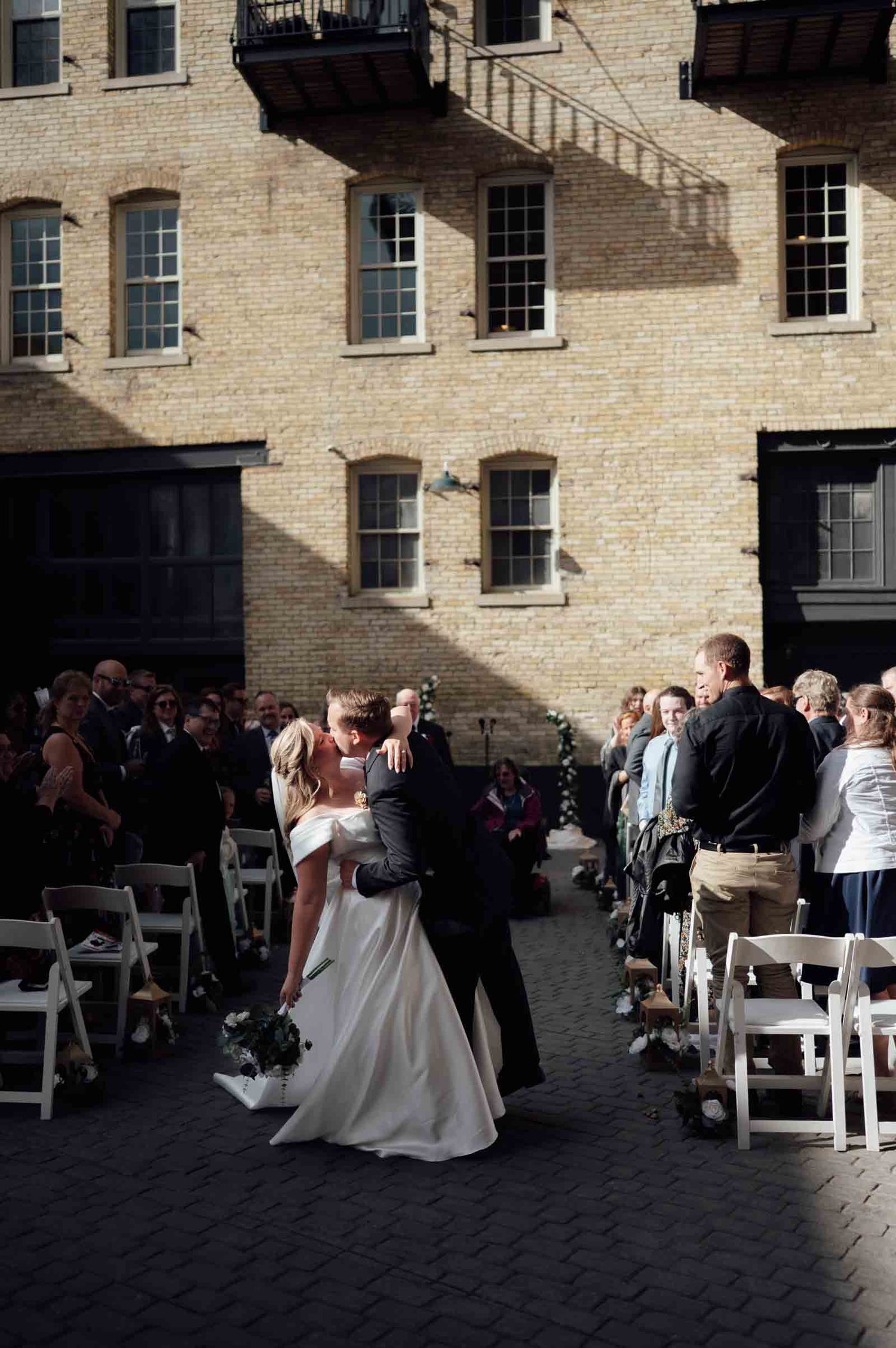 Bride and groom sharing a kiss while walking down the aisle at an outdoor courtyard wedding ceremony.
