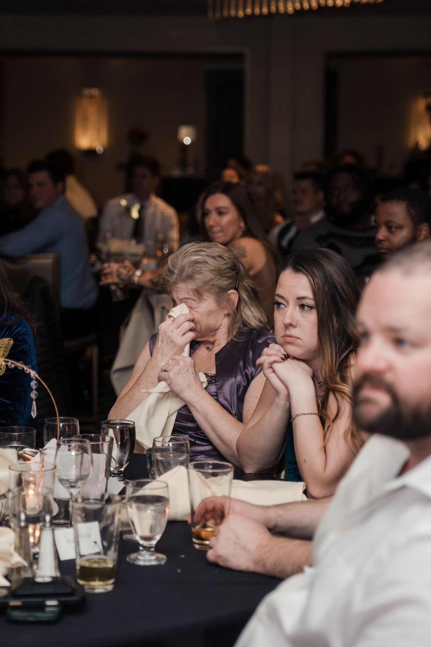 Wedding guests seated at tables during reception dinner in a dimly lit banquet hall.