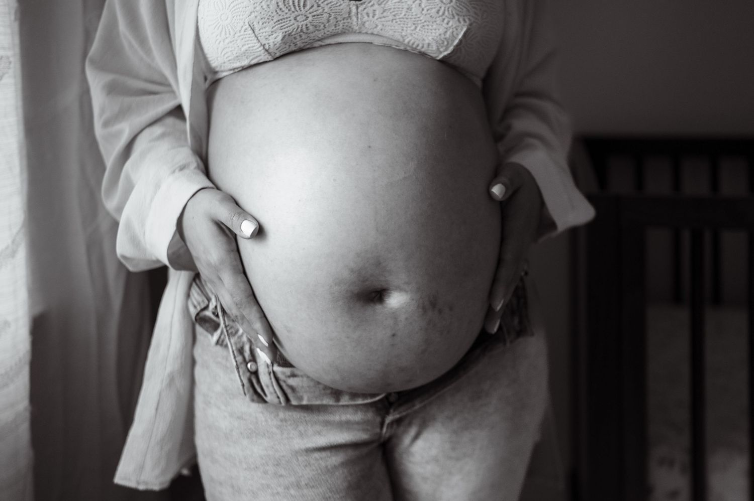 Black and white photo of tattooed pregnant belly with hands resting gently on both sides.