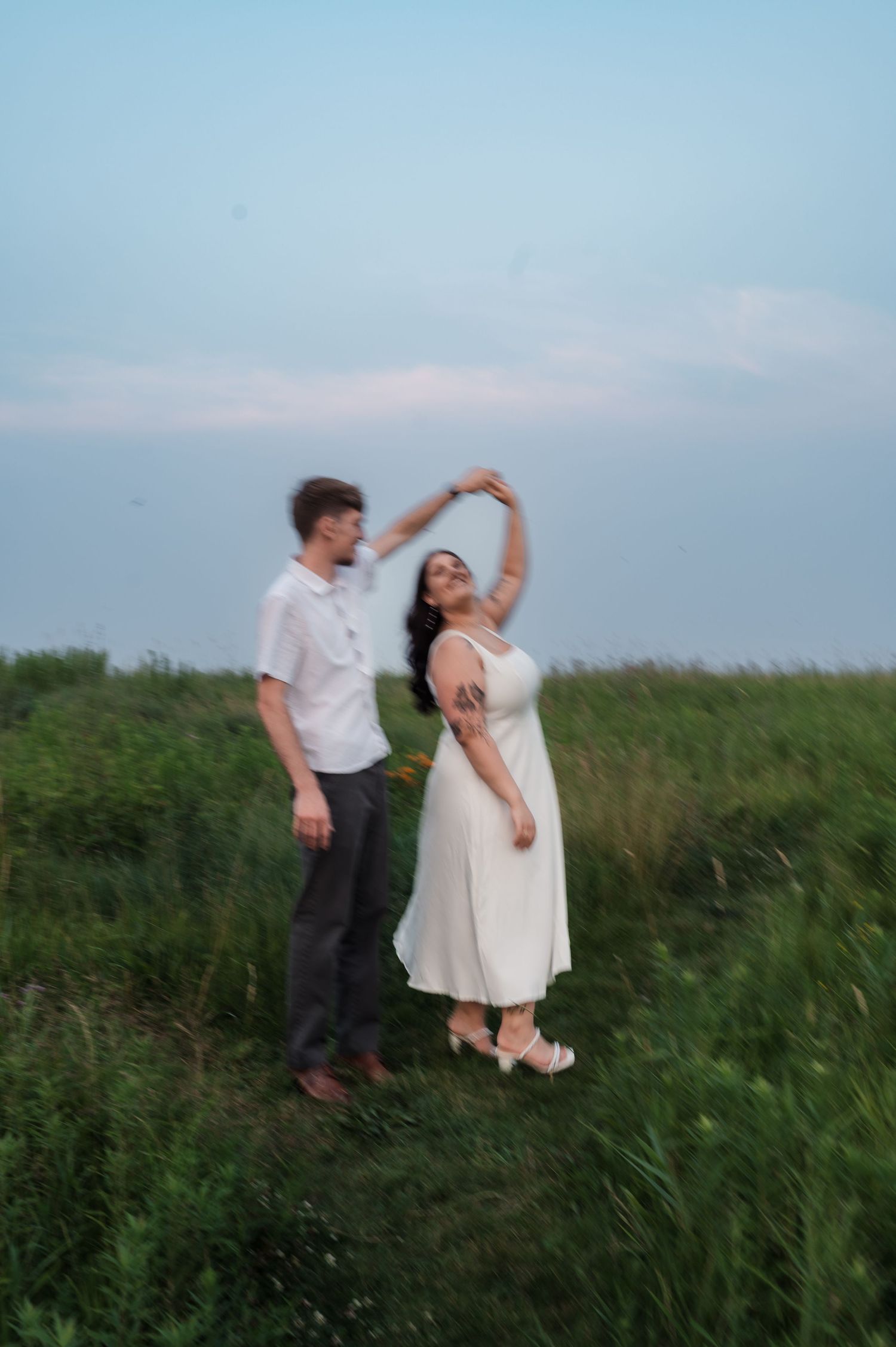 A couple dances together in a grassy meadow against a blue sky.