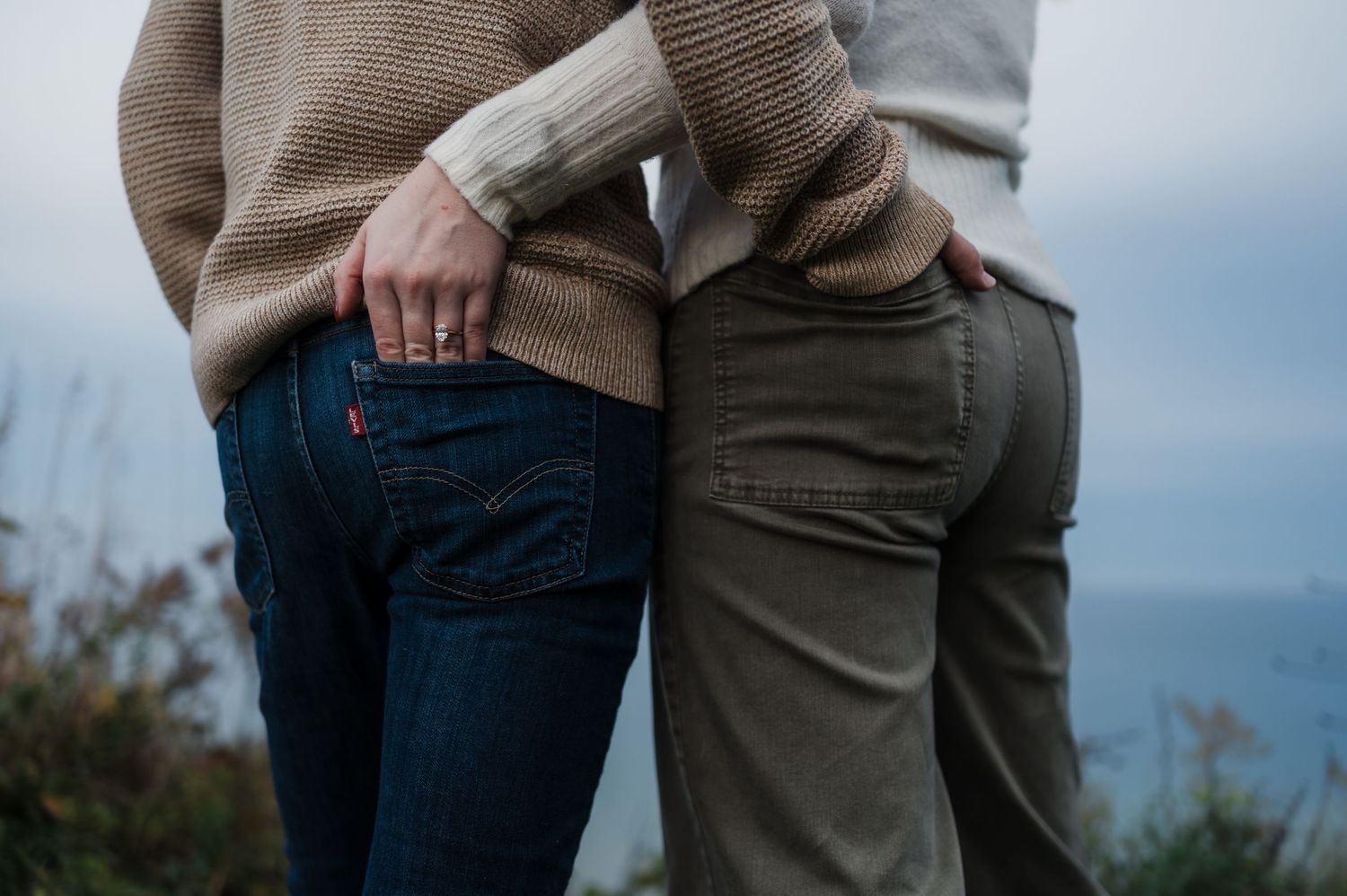 Close-up of an engaged couple standing side by side outdoors, showcasing a diamond engagement ring.