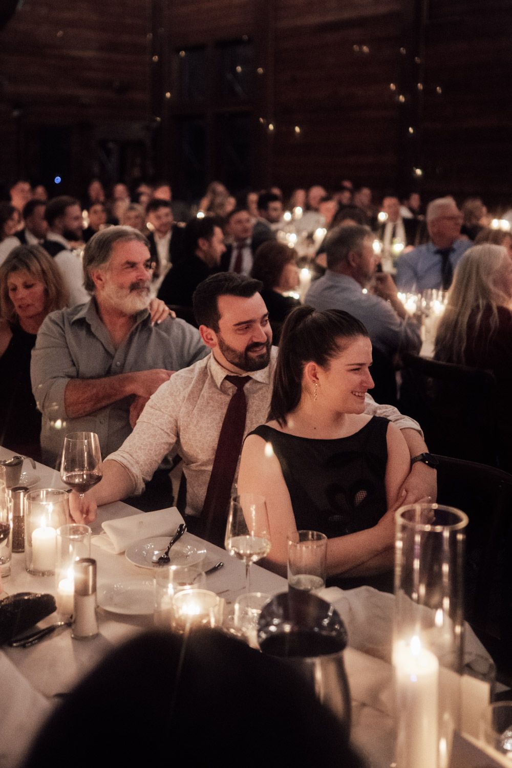 Wedding guests smiling and enjoying candlelit reception dinner in rustic barn venue.