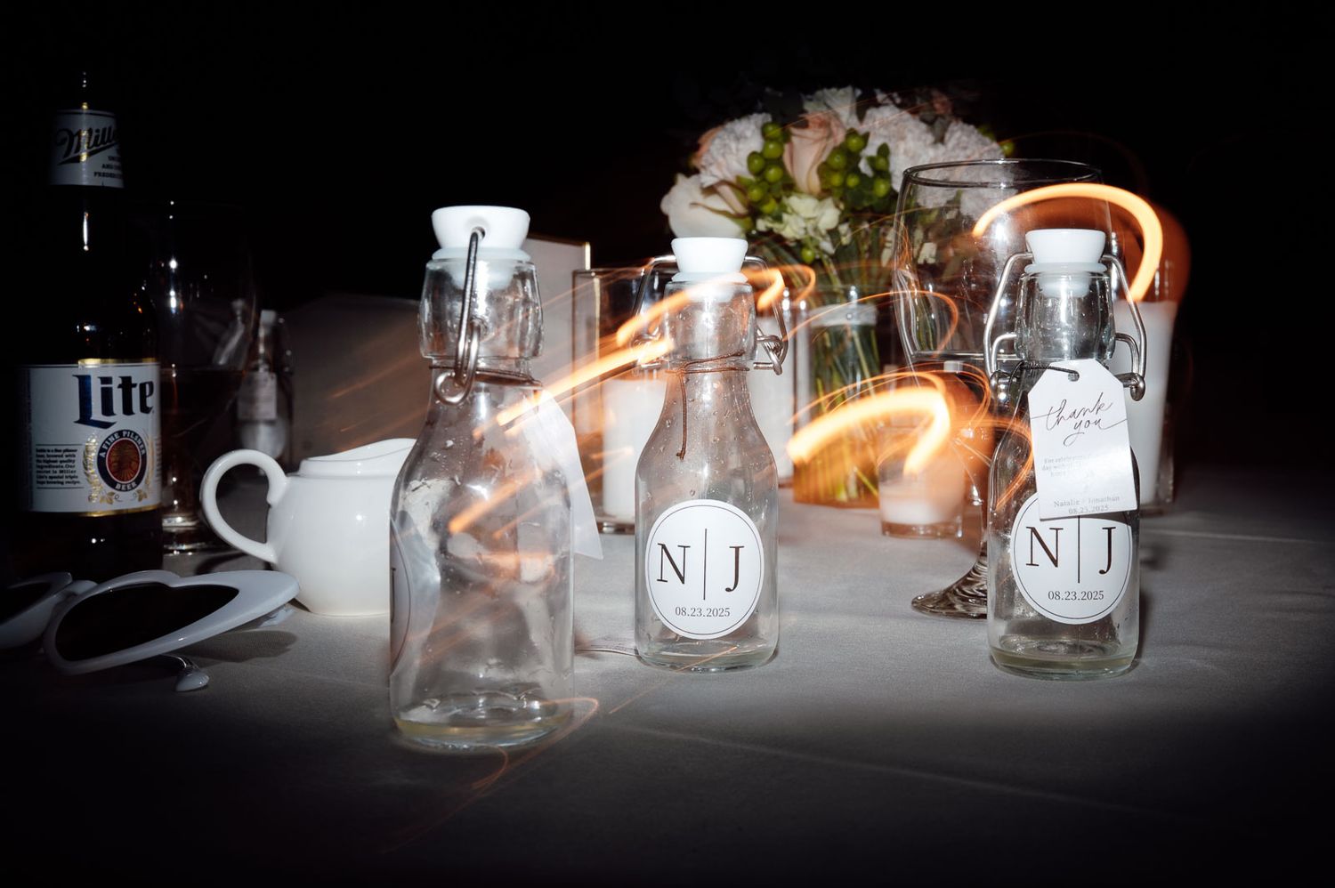 Personalized NJ monogram glass bottles displayed as wedding favors on a reception table.