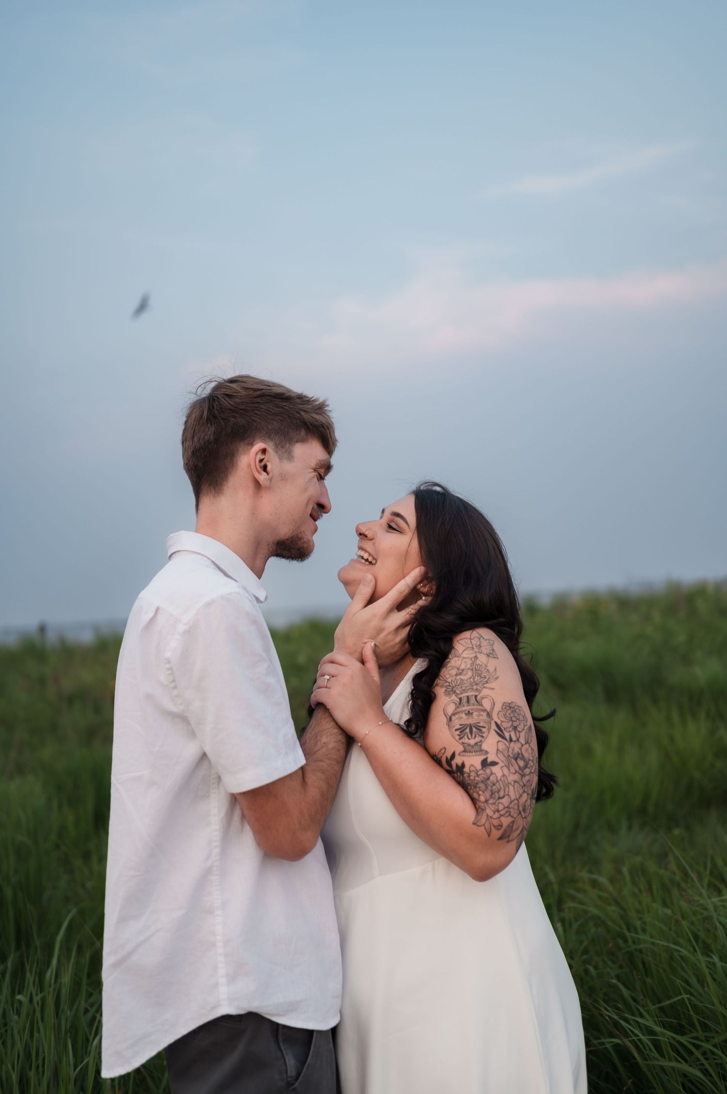 A couple shares an intimate moment together while standing in a green field during sunset.