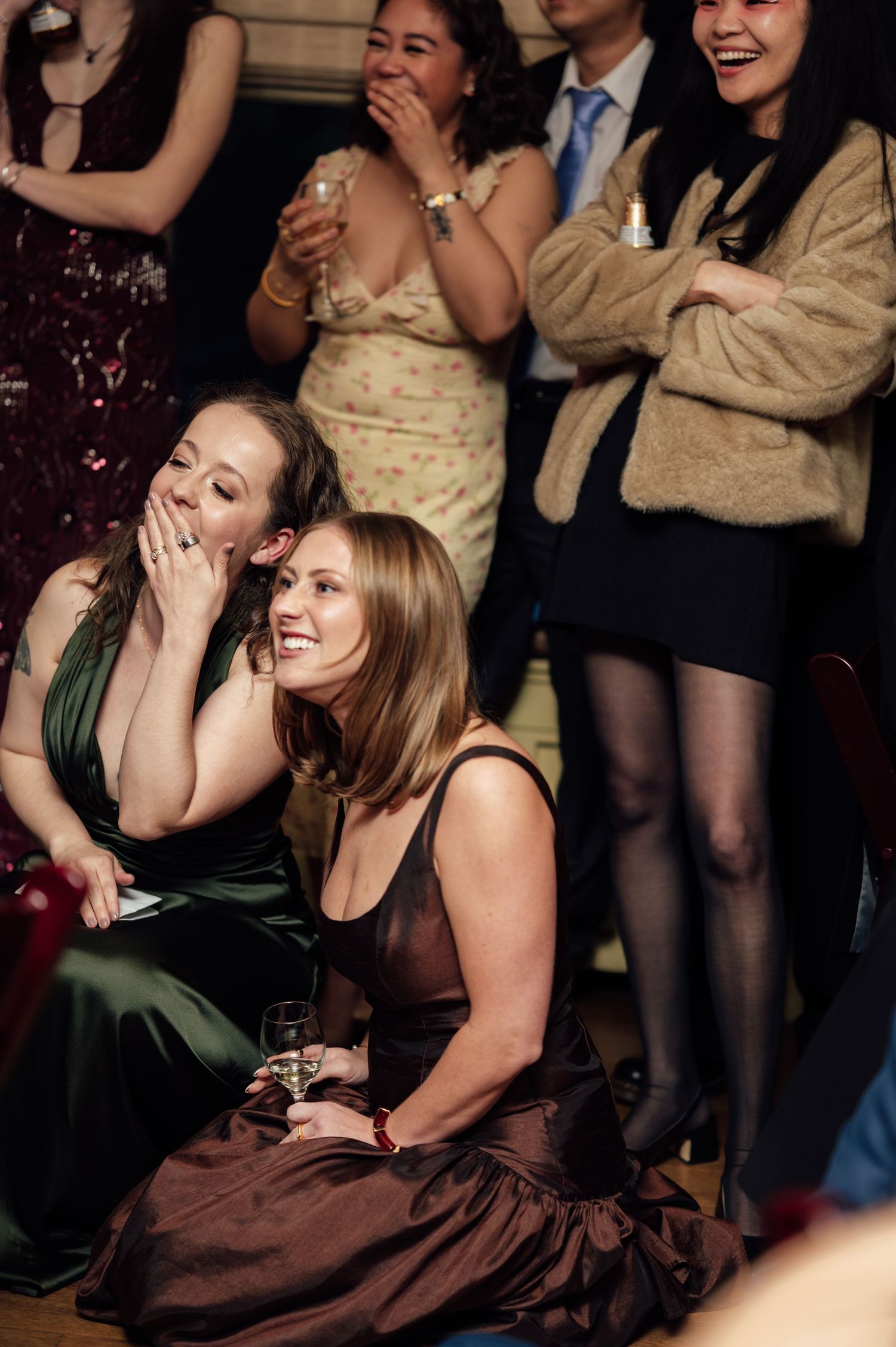 Guests laughing and enjoying themselves at a wedding reception, women in elegant dresses seated on the floor.