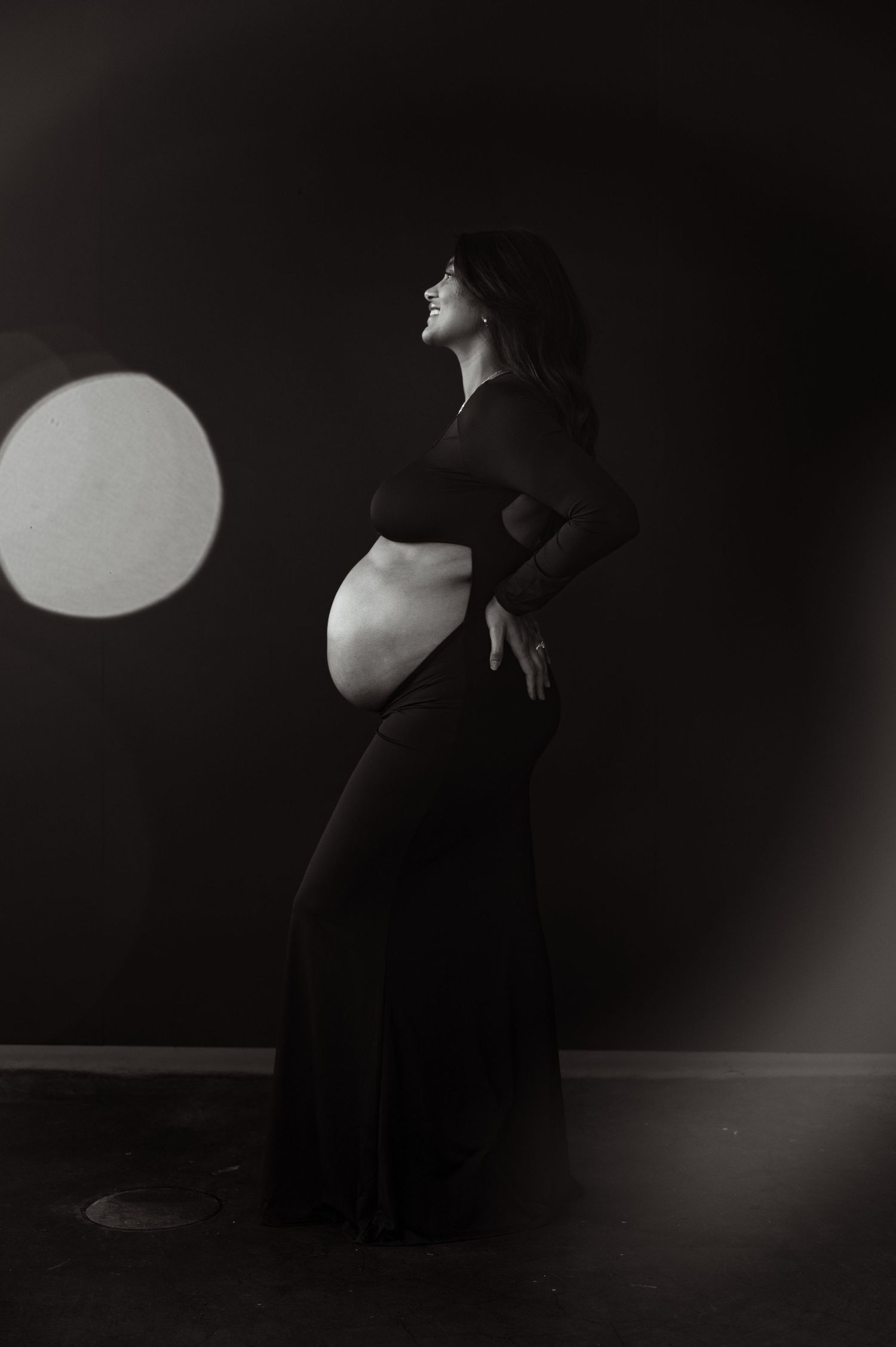 Black and white silhouette of pregnant woman in black gown with circular light.