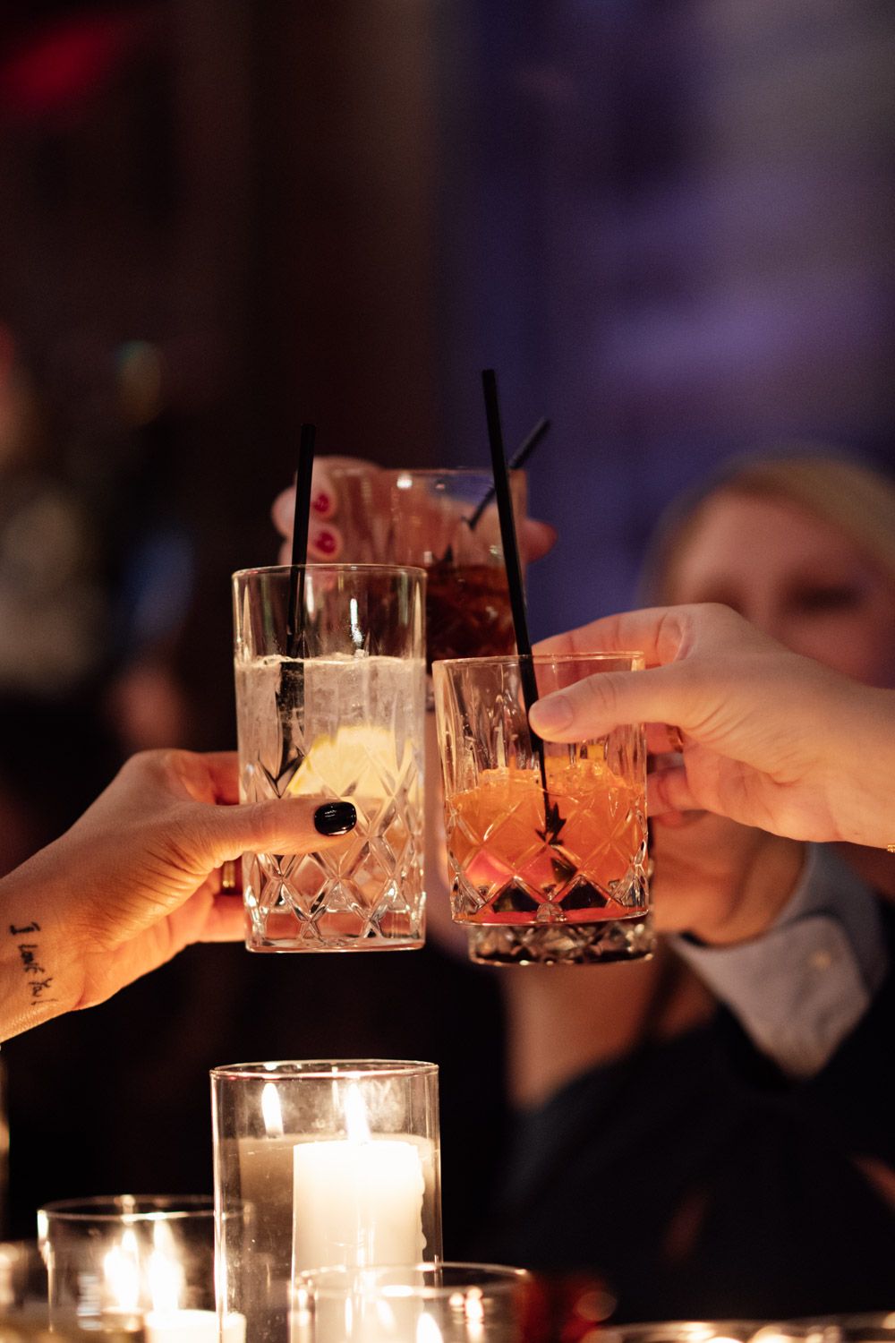 Wedding guests clinking crystal cocktail glasses in celebratory toast by candlelight.