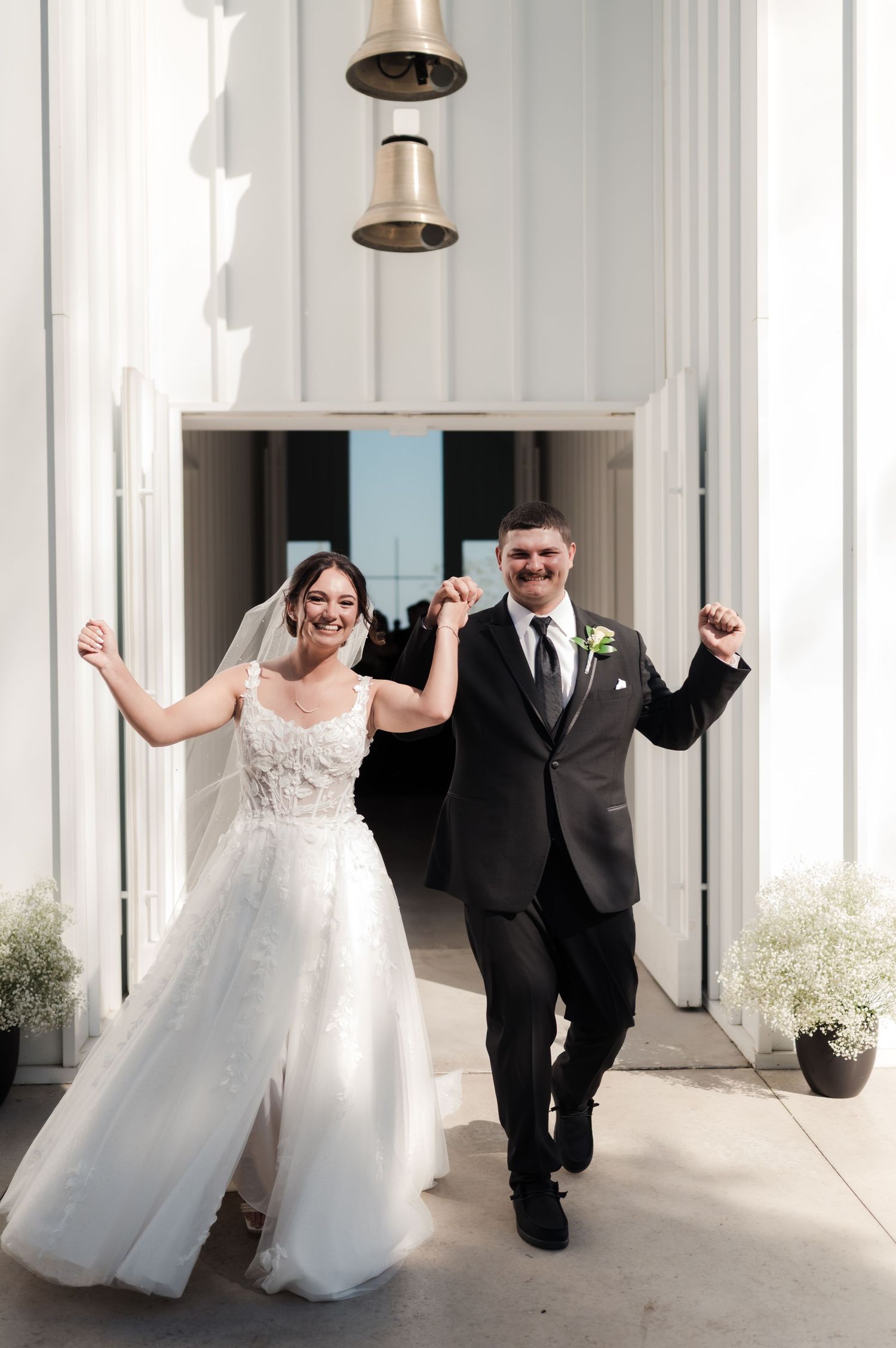 Bride and groom celebrating joyfully as they exit a bright white chapel after their ceremony.