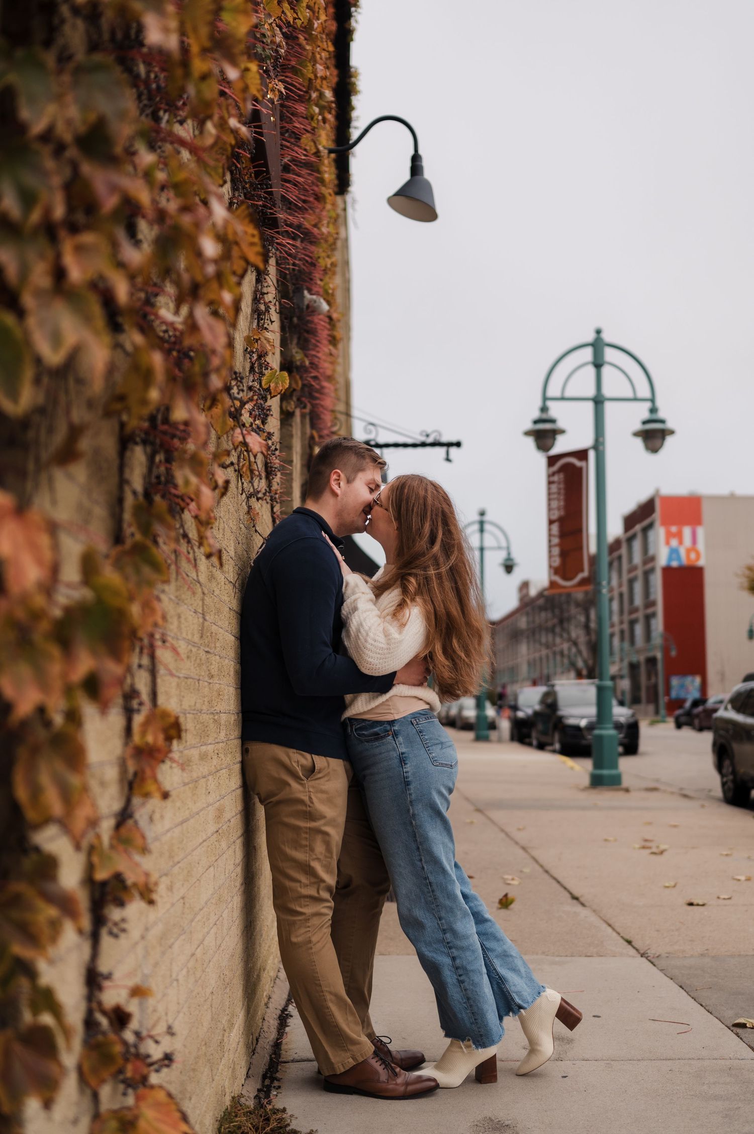 Couple sharing a tender moment against an ivy-covered brick wall on a charming city sidewalk.