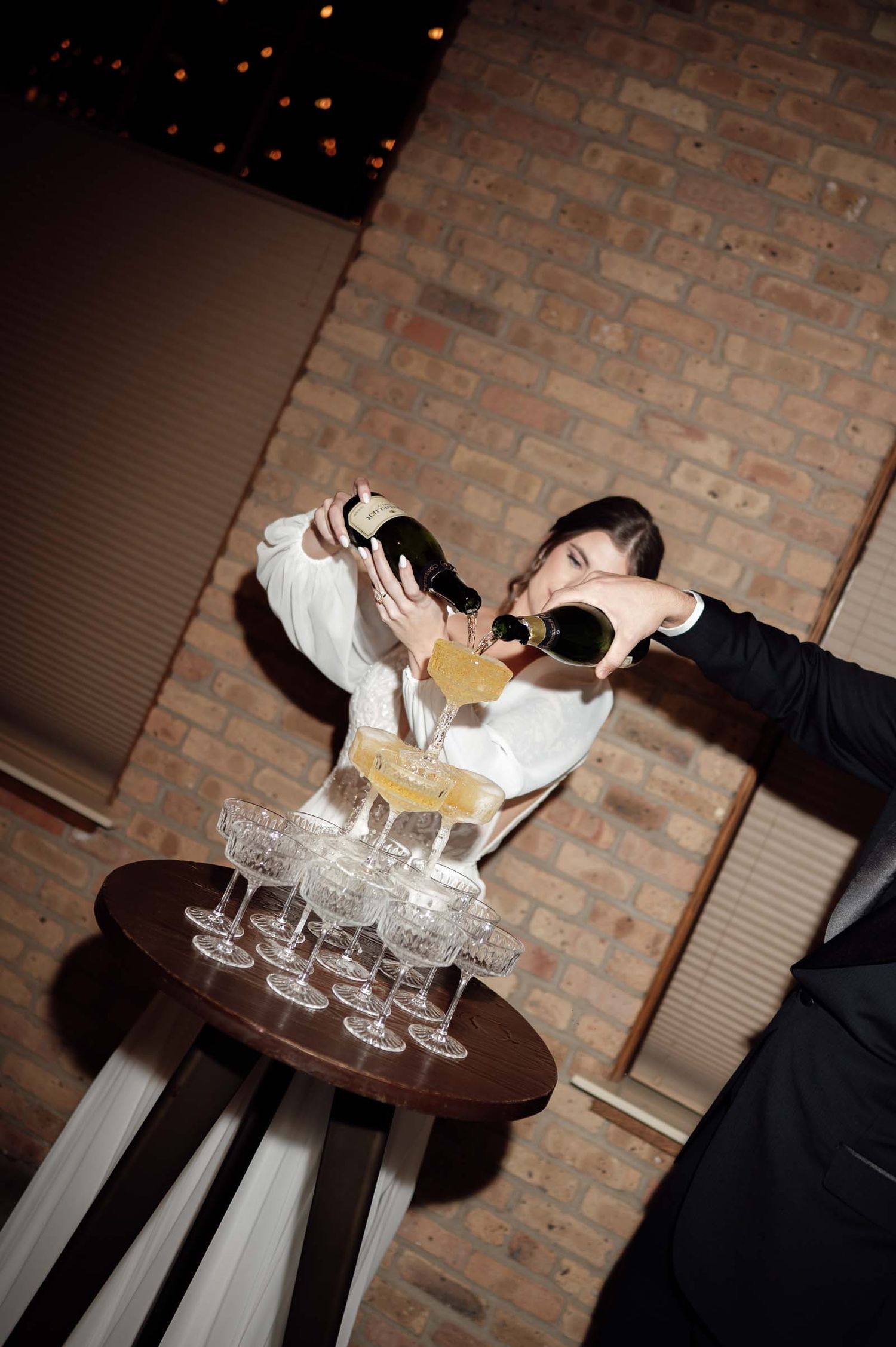 Bride and groom pour champagne together over a elegant tower of crystal glasses at wedding reception.