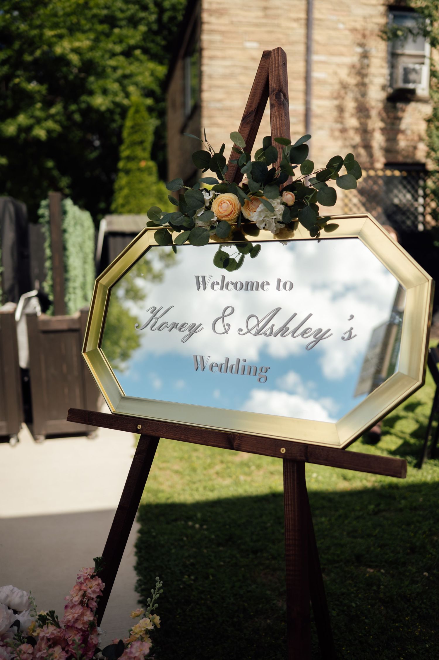 Gold octagonal mirror wedding welcome sign for Korey & Ashley's wedding, decorated with eucalyptus and roses on a wooden easel.
