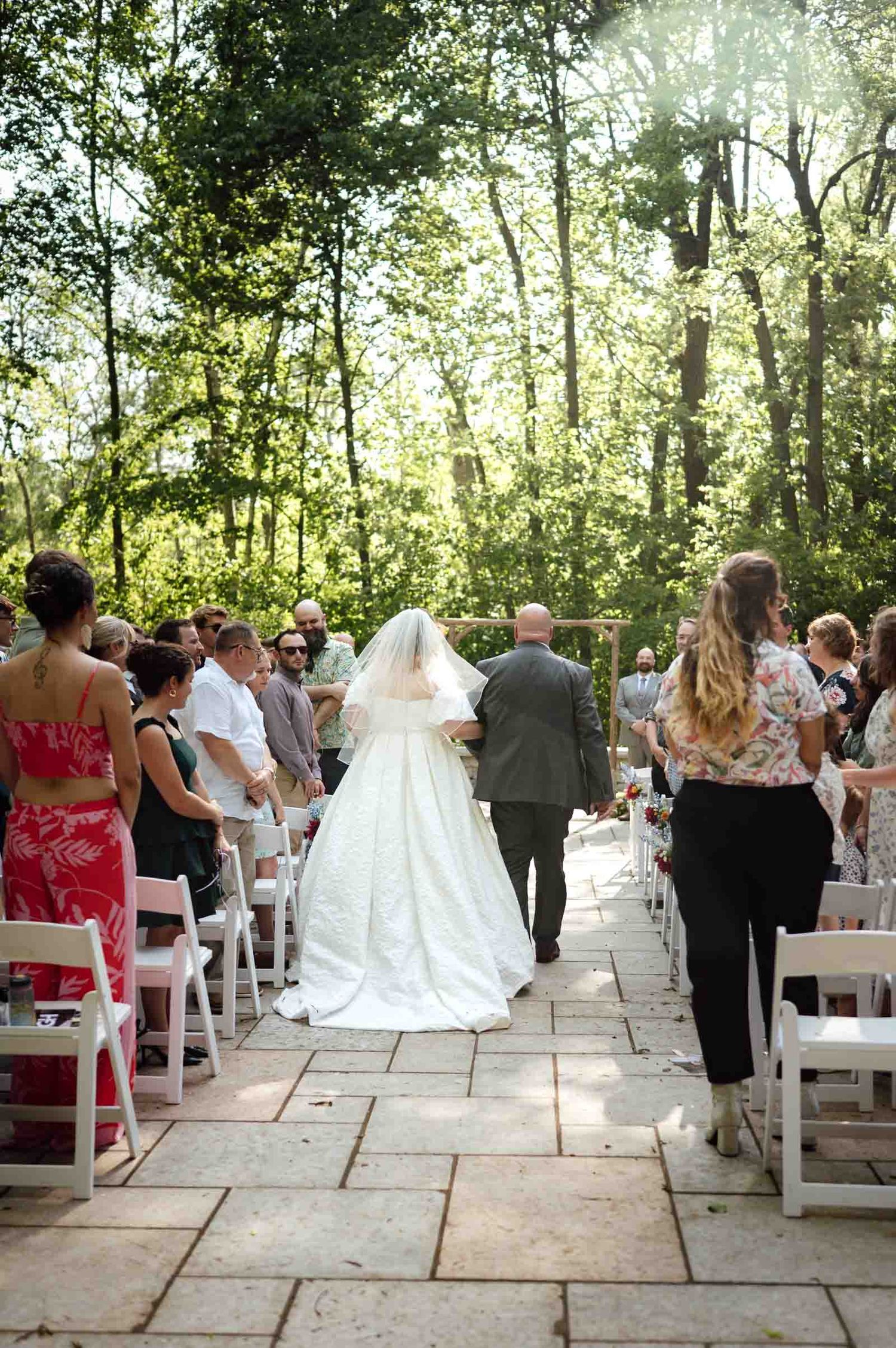 Bride walking down outdoor stone aisle with escort at garden wedding ceremony.