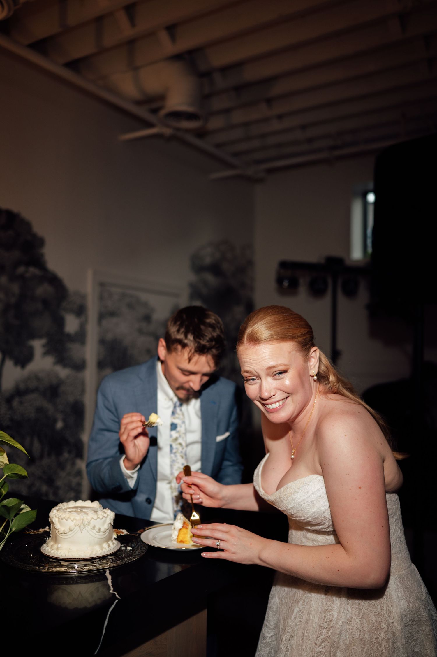 Bride and groom smiling while cutting their white wedding cake at their indoor reception venue.