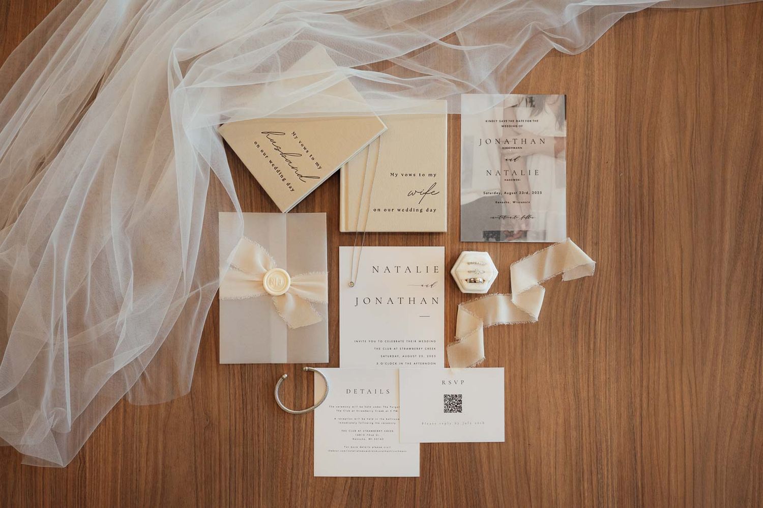 Elegant wedding invitation suite with gold accents, rings, and veil on a wooden surface.