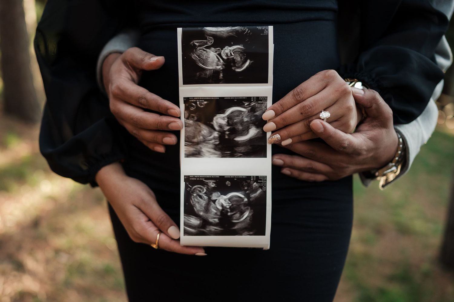 Couple holding ultrasound photos against a baby bump during an outdoor maternity announcement shoot.