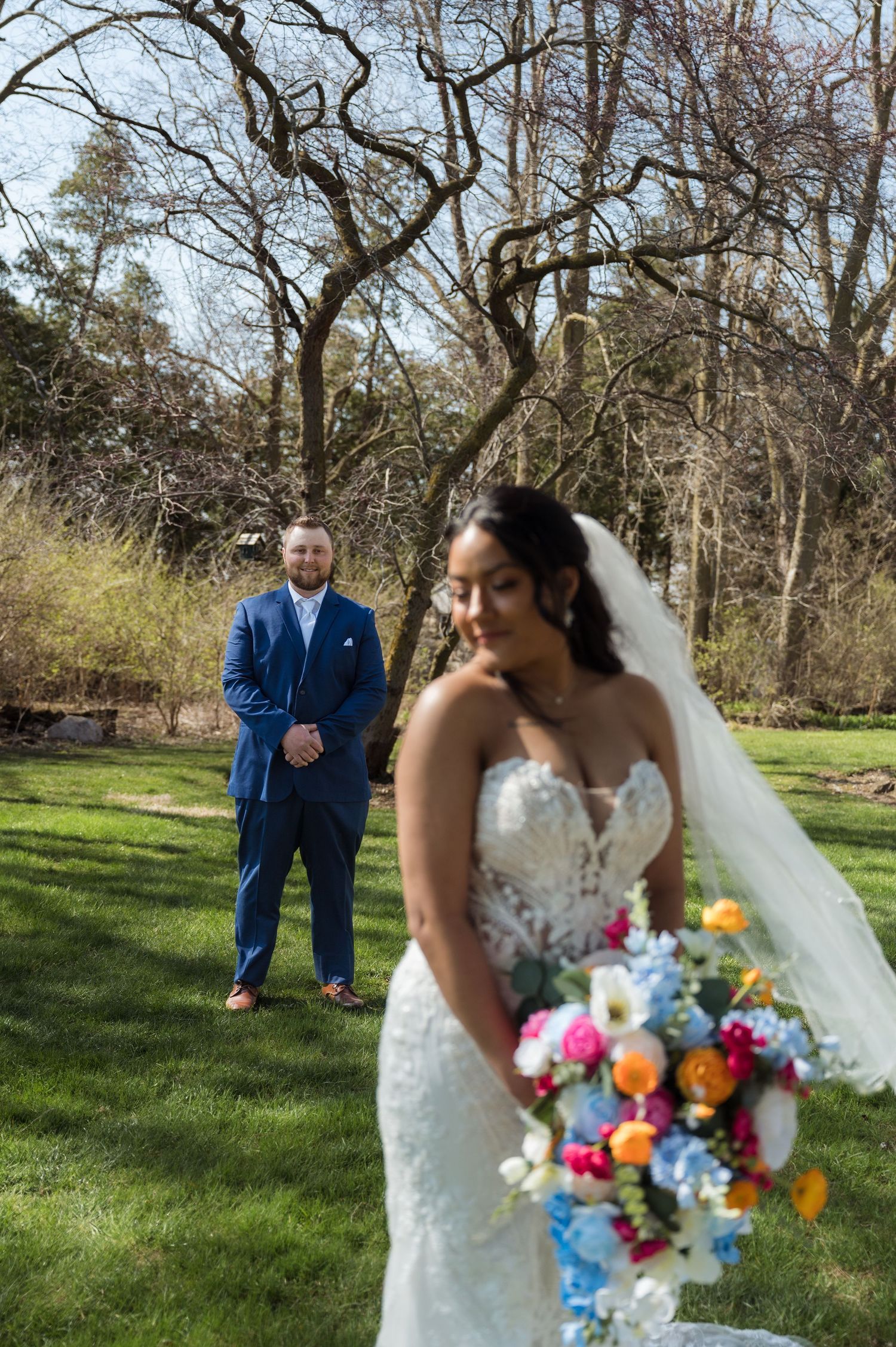 Wedding photo in a garden setting with a beautiful white lace dress and vibrant multicolored bouquet in spring.