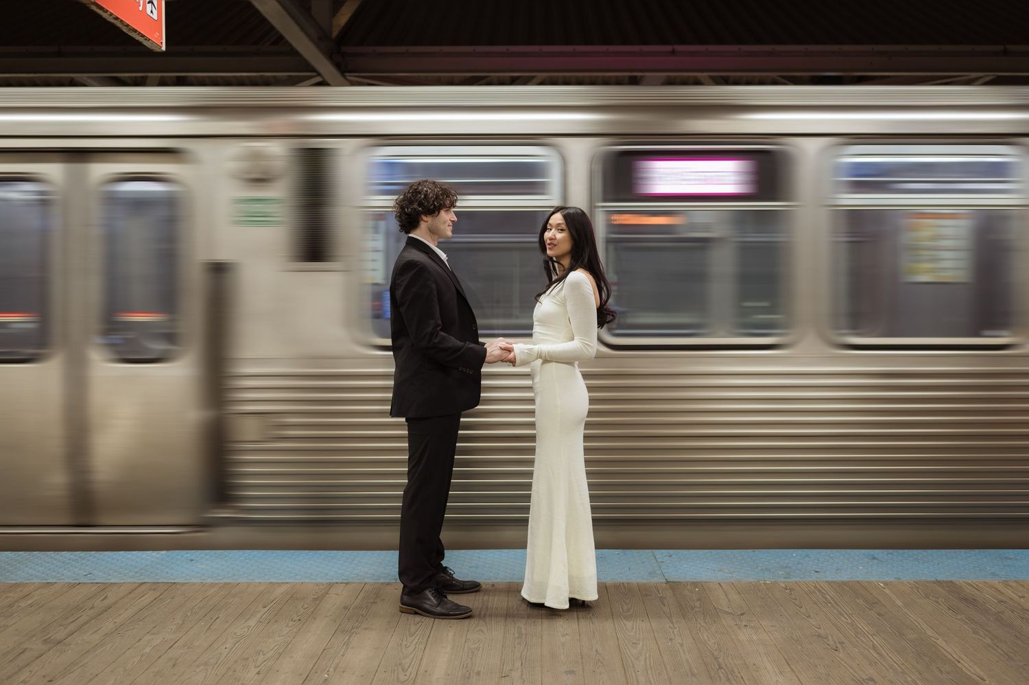 Couple holding hands on a Chicago subway platform with a blurred train passing behind them.