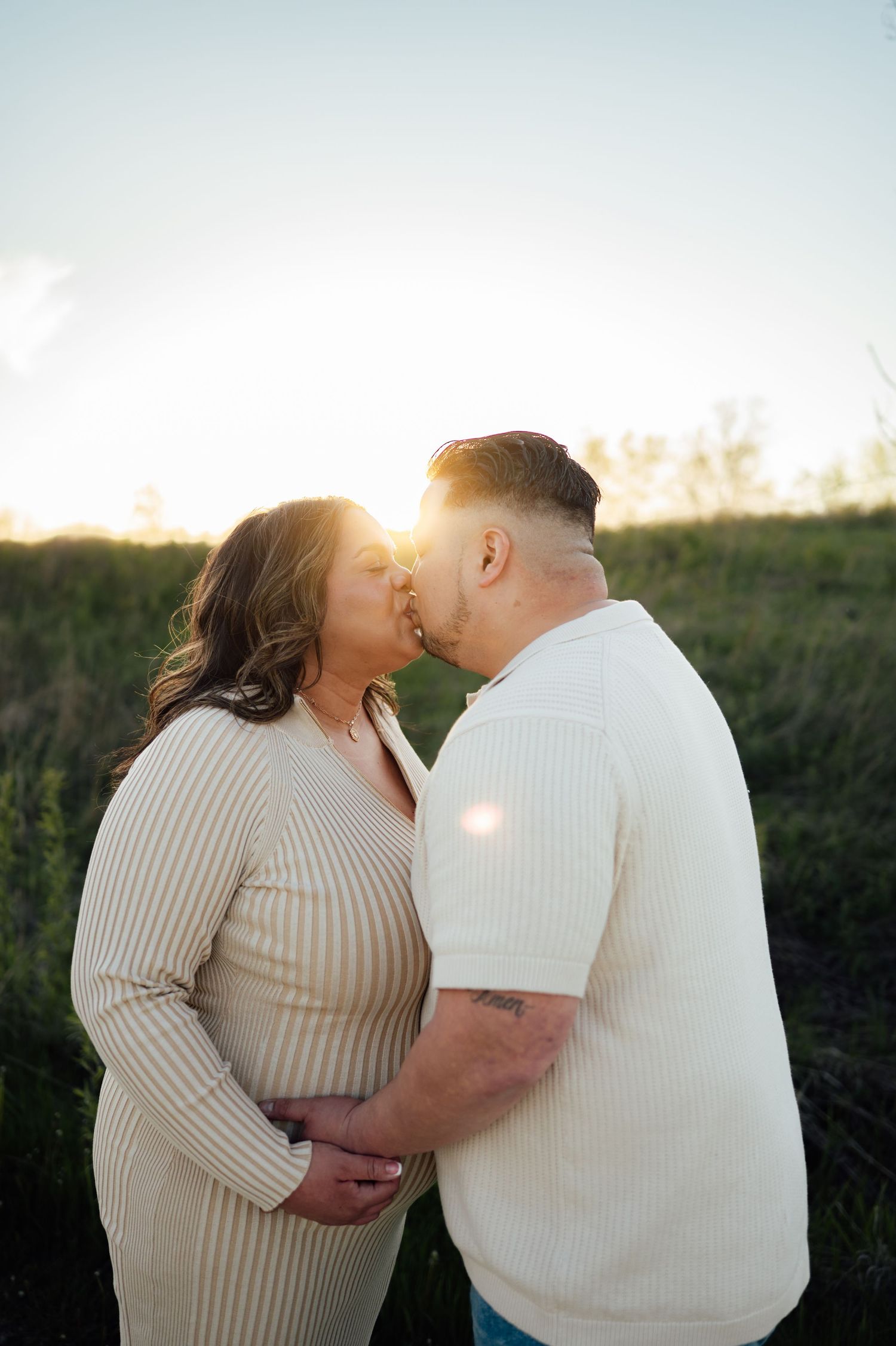 Expecting couple sharing a kiss at golden hour in a green field.