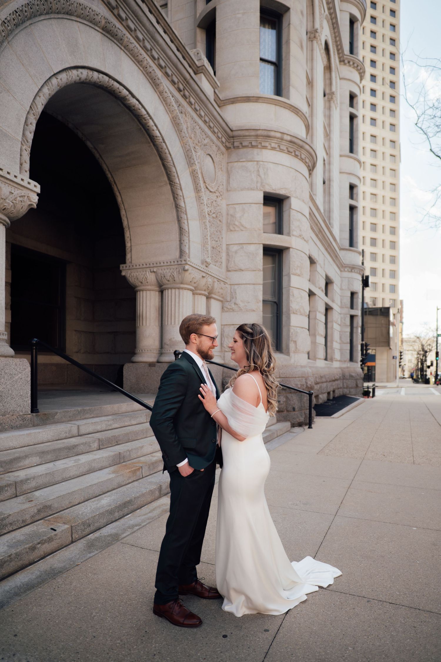 Bride and groom share a romantic moment outside a grand stone building on their wedding day.
