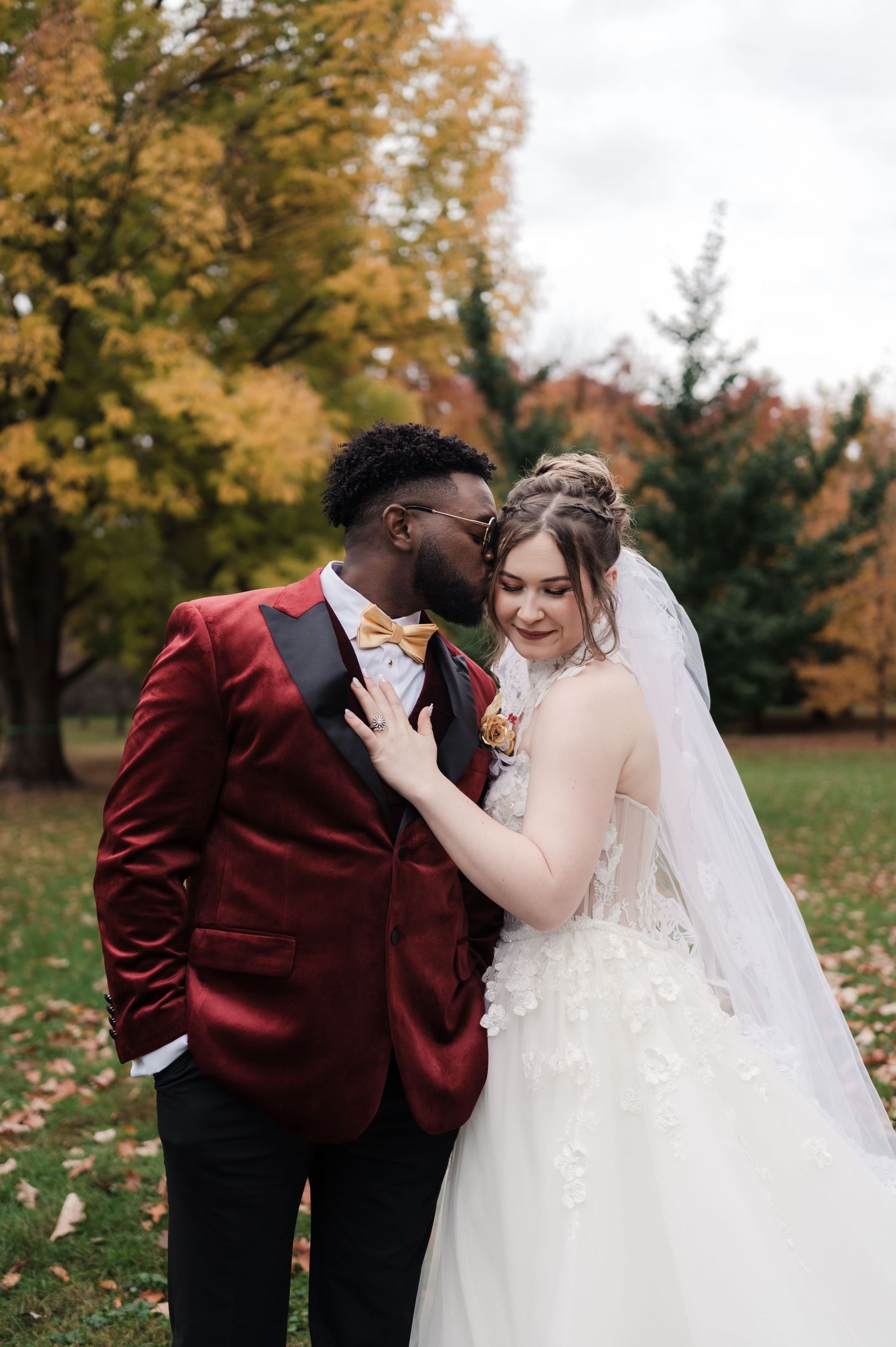 A romantic wedding photoshoot in an autumn setting with falling leaves and golden trees in the background.