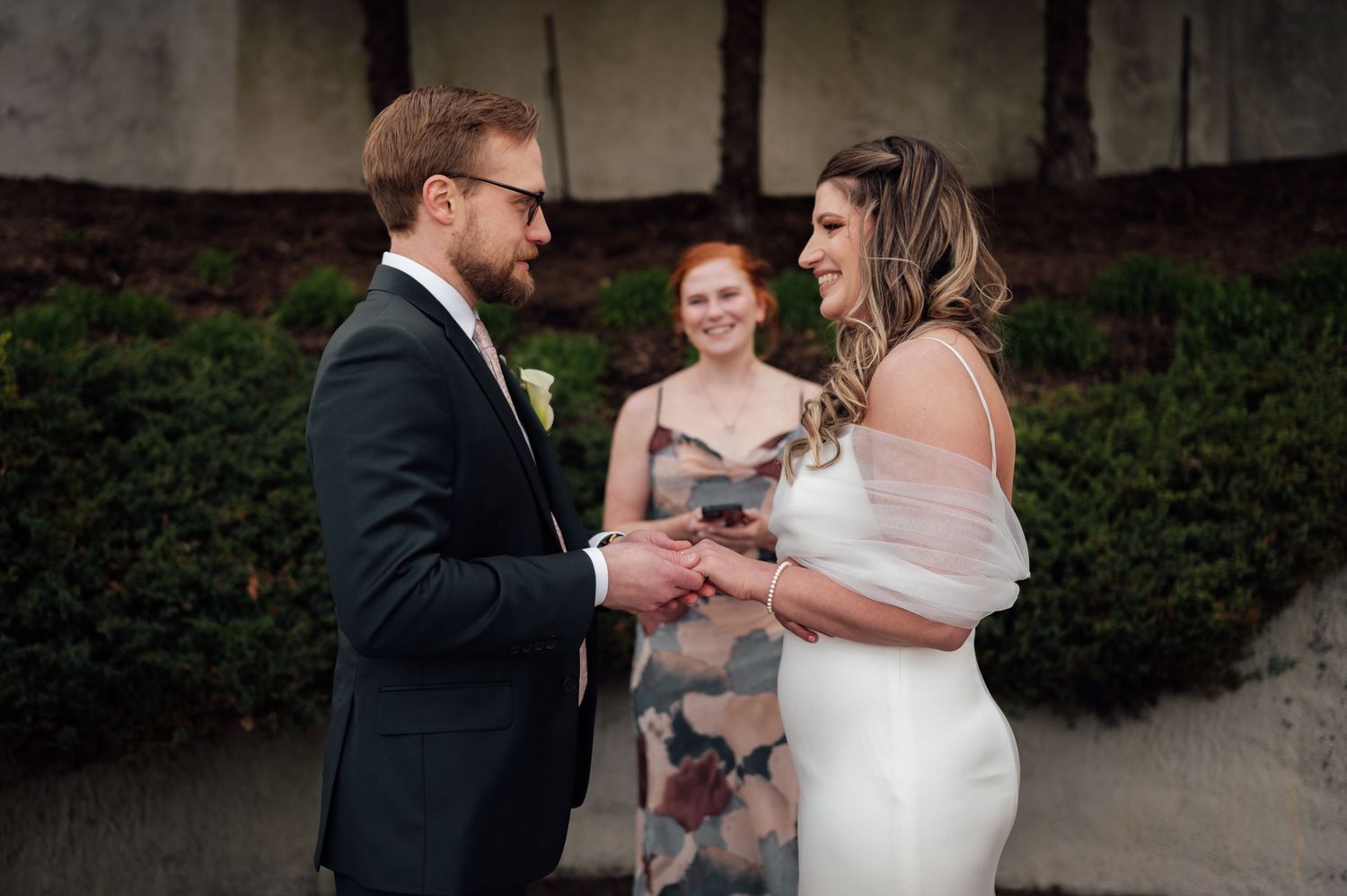 Bride and groom exchanging vows with smiling officiant during an outdoor wedding ceremony.