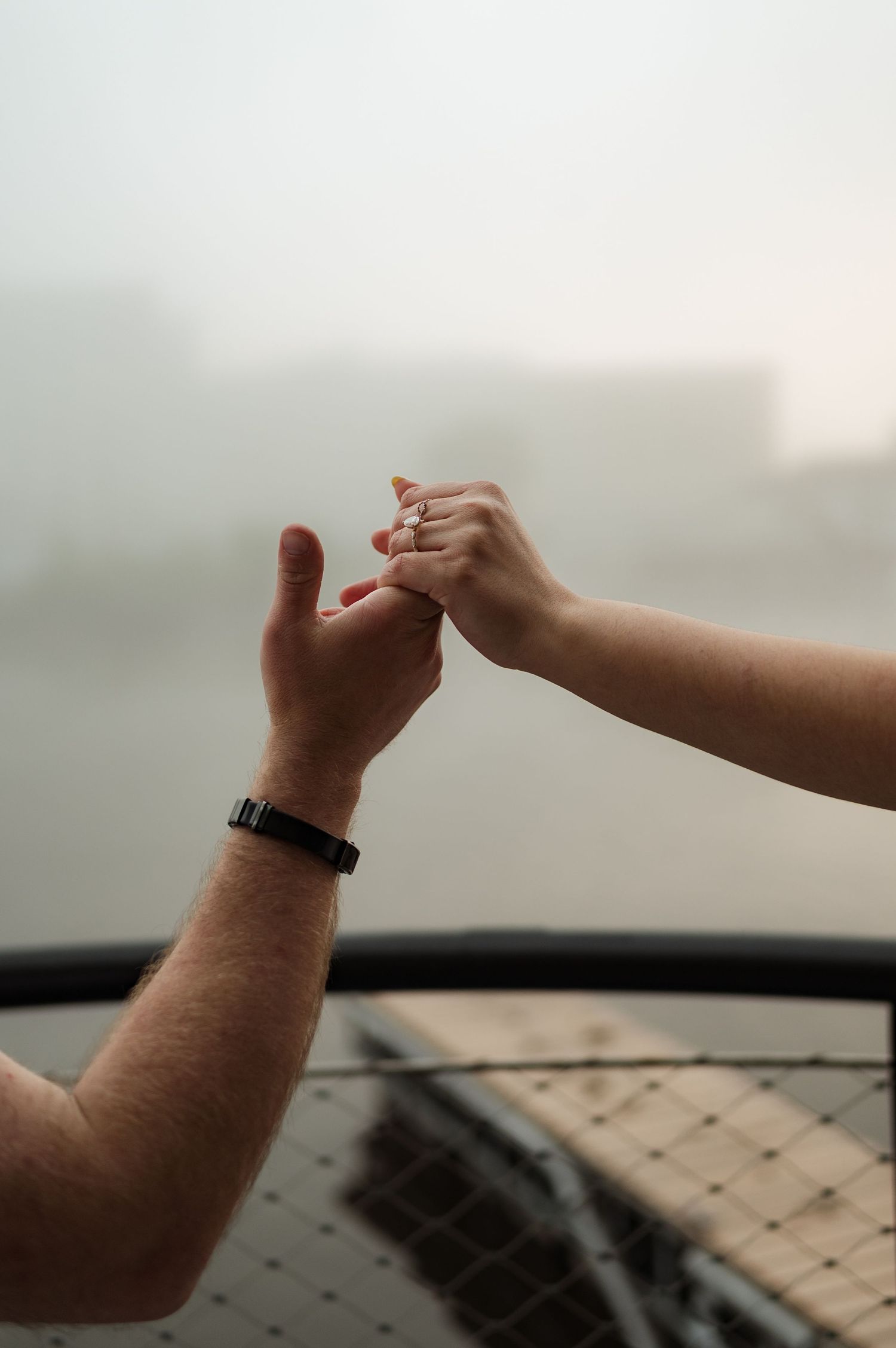 Close-up of a couple holding hands on a misty waterfront, man wearing a black watch.