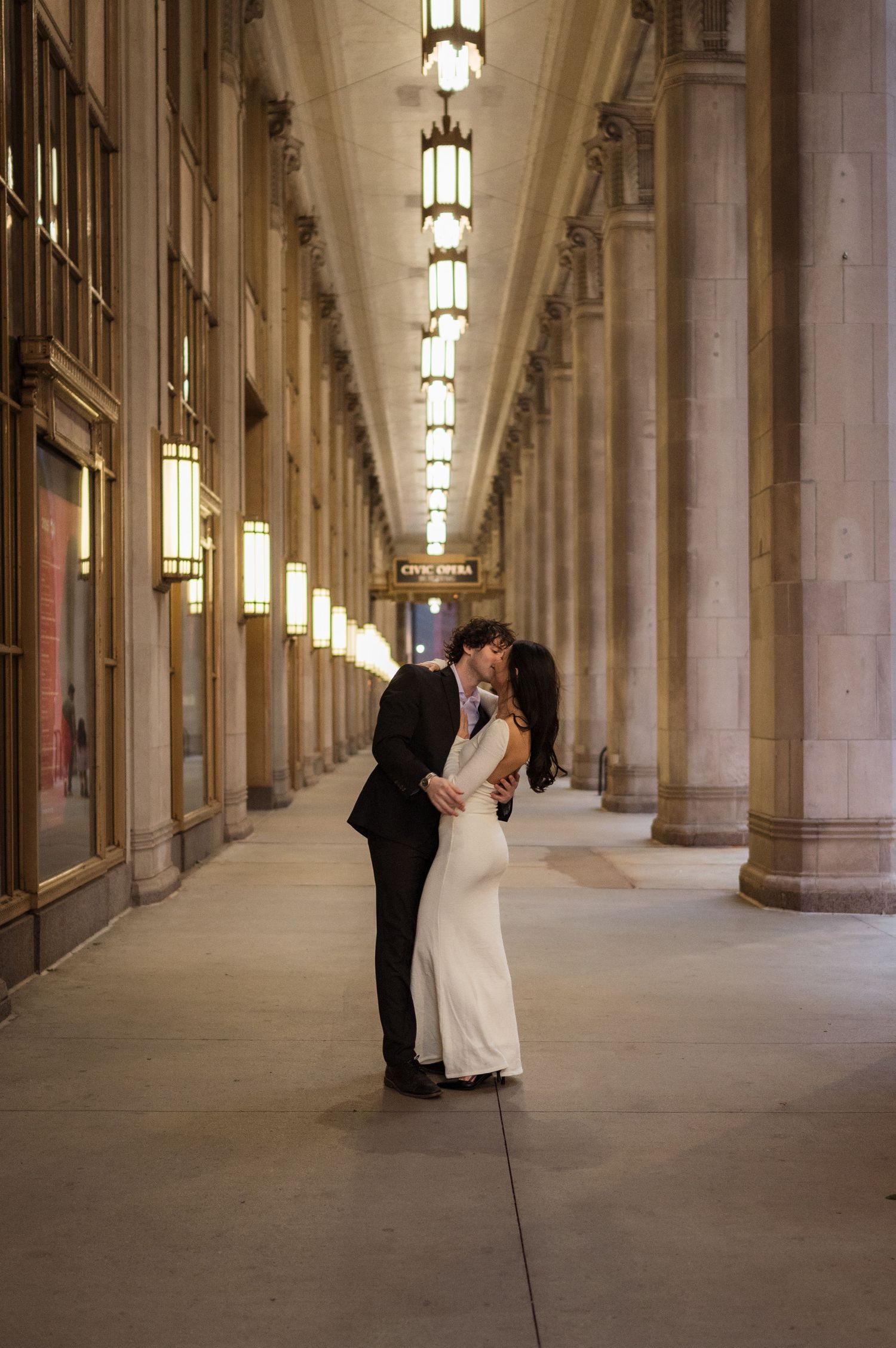 Couple sharing a romantic kiss in an elegant Chicago building arcade with ornate columns and warm lighting.
