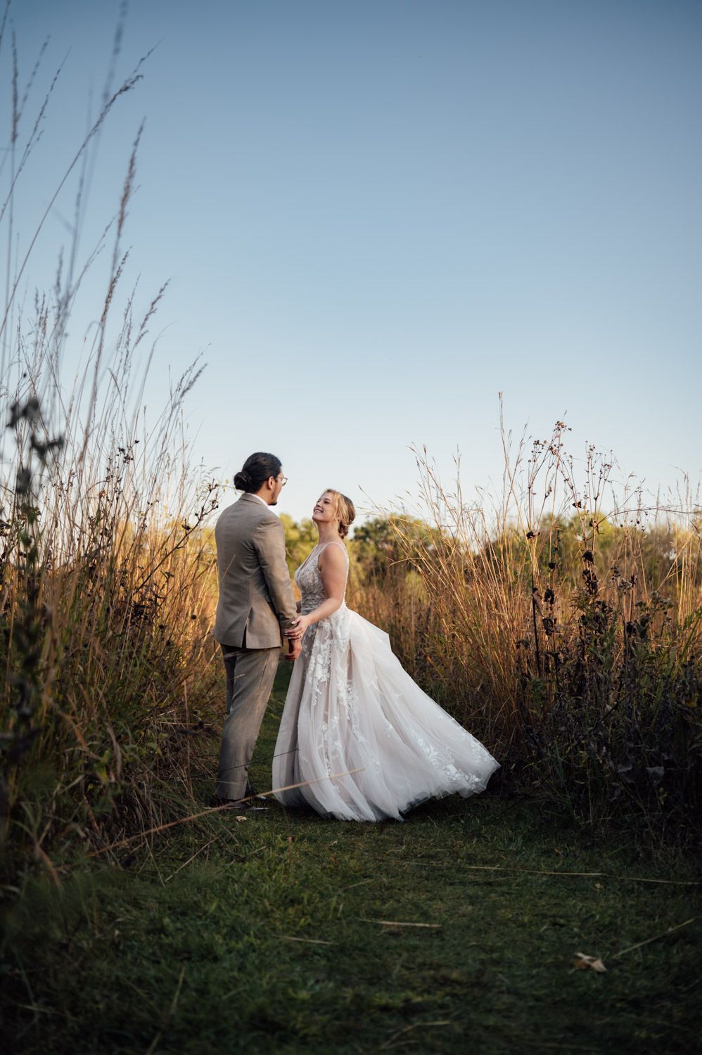Bride and groom holding hands in golden field at sunset during outdoor wedding portrait.