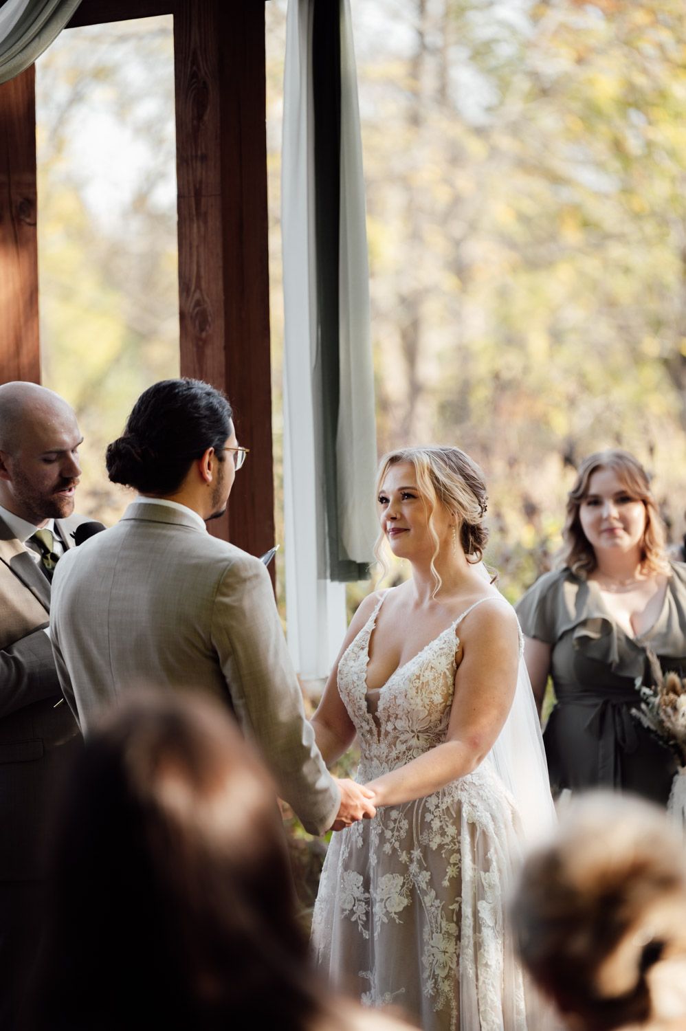 Bride smiling at groom during indoor wedding ceremony while holding hands at the altar.